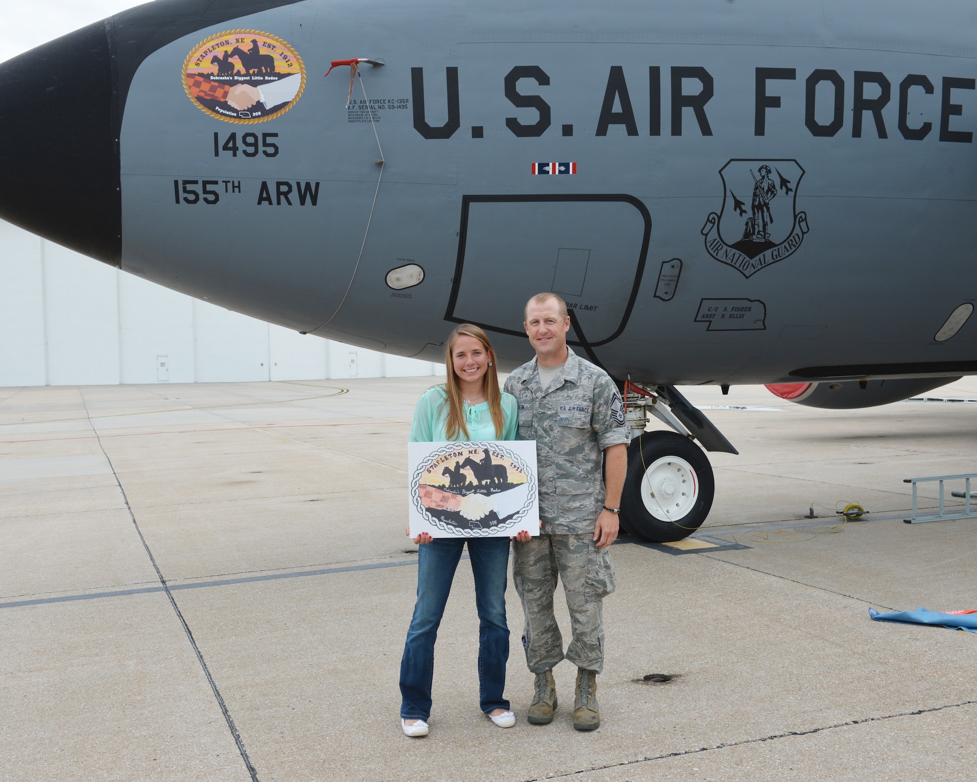 Mariah Harm, a Stapleton, Neb., native and senior at Stapleton High School, holds her original artwork submission with Senior Master Sgt. Chad Martin, the director of the Nebraska Community Nose Art Program, after she unveiled her artwork on the nose of a KC-135R Stratotanker at the 155th Air Refueling Wing, Nebraska Air National Guard Base Aug. 8, in Lincoln, Neb.