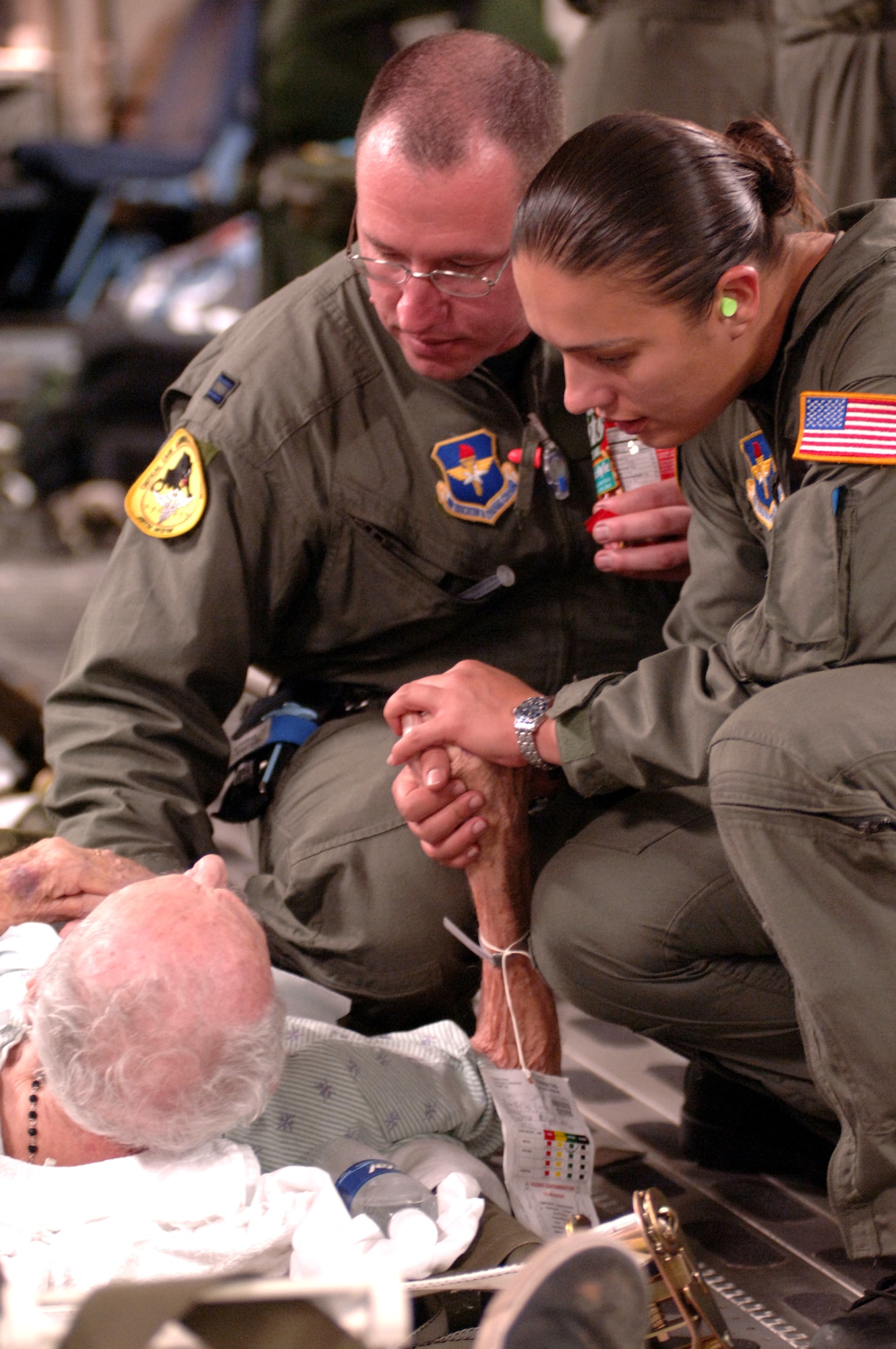 Capt. Mike Dixon, ICU nurse with the 59th Medical Wing and Staff Sgt. Lina Gamez , respiratory therapist with the 759th MSGS, provide a hand to hold and reassuring words to an elderly patient and survivor of hurricane Katrina.  They are traveling, om 1 Sept. 2005, aboard a C-17 Globemaster III assigned to the 446th Airlift Squadron, McChord Air Force Base.  Dixon and Gamez are stationed at Lackland Air Force Base, TX, and have teamed up with the activated Reserve crew from McChord to provide aeromedical evacuation for ambulatory and critical care patients in New Orleans.  This 1.5 hour flight carried 28 ambulatory and 6 litters to Dobbins Air Force Base, GA. (U.S. Air Force photo Master Sgt. Lance Cheung)