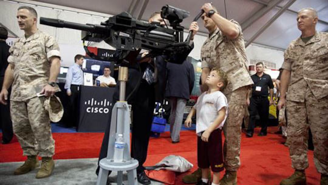Maj. John R. Bitonti II, Headquarters and Service Battalion, helps his son try out the latest weapon technology on display during the Modern Day Marine Military Exposition at Marine Corps Base Quantico, Va., Sept. 29. Although many of the products were not currently in use by the Corps, the exposition gave vendors the opportunity to promote their products to Marines.
