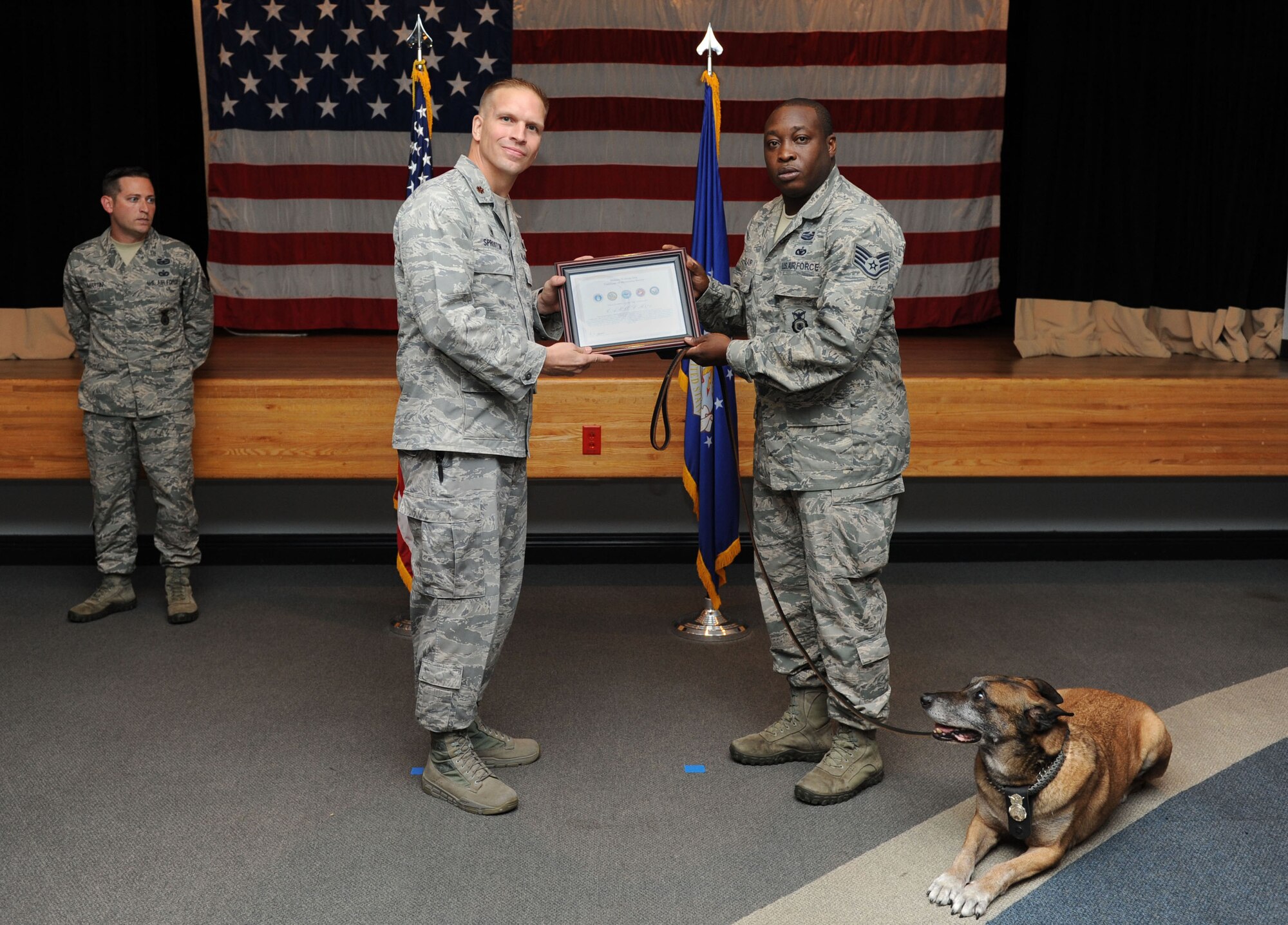 Maj. Devin Sproston, 81st Security Forces Squadron commander, presents a retirement certificate to Staff Sgt. Garth St. Clair, 81st SFS military working dog handler, on behalf of Carlos, 81st SFS military working dog, during a retirement ceremony for Carlos Sept. 16, 2015, at the Don Wylie Auditorium, Keesler Air Force Base, Miss. Carlos was in the service for 11 years and served deployments in Afghanistan with a Navy SEAL unit; Iraq with a U.S. Army unit and three deployments with St. Clair. He has been adopted by St. Clair. (U.S. Air Force photo by Kemberly Groue)
