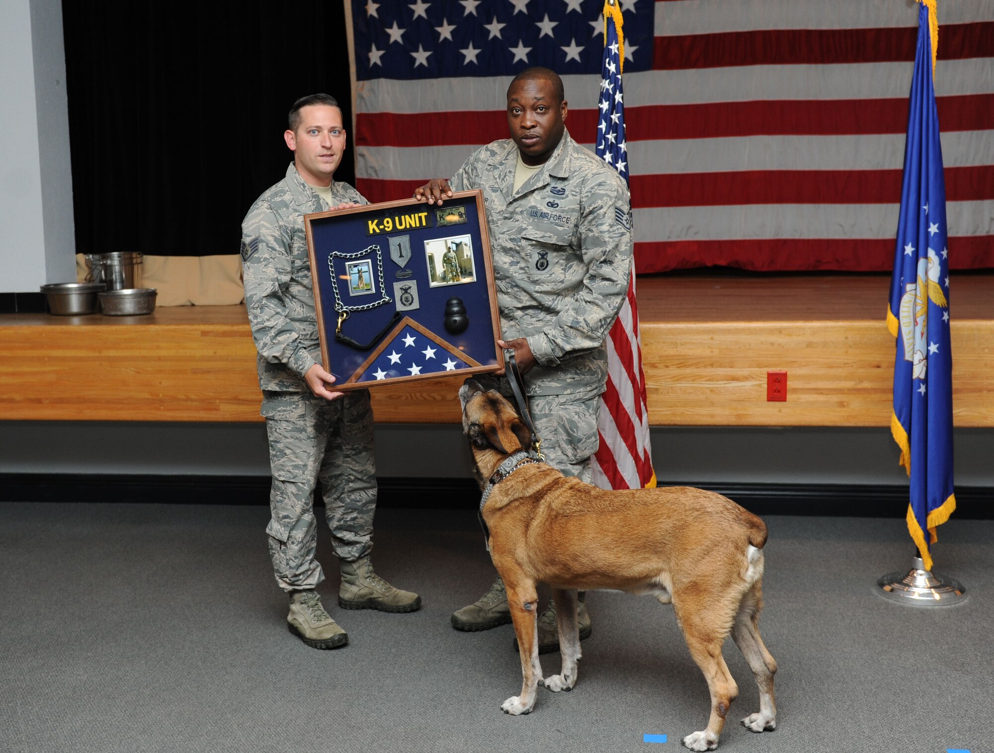Staff Sgt. James Martin, 81st Security Forces Squadron kennel master, presents a shadow box to Staff Sgt. Garth St. Clair, 81st SFS military working dog handler, on behalf of Carlos, 81st SFS military working dog, during a retirement ceremony for Carlos Sept. 16, 2015, at the Don Wylie Auditorium, Keesler Air Force Base, Miss. Carlos was in the service for 11 years and served deployments in Afghanistan with a Navy SEAL unit; Iraq with a U.S. Army unit and three deployments with St. Clair. He has been adopted by St. Clair. (U.S. Air Force photo by Kemberly Groue)