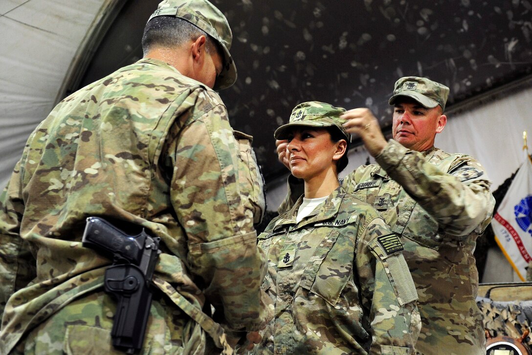U.S. Navy Command Senior Chief James Fyfe, left, pins anchors on Chief Hospital Corpsman Jessica Guzman, center, while U.S. Navy Command Master Chief Keith W. Metcalf, right, places her cover during a chief pinning ceremony on Bagram Airfield, Afghanistan, Sept. 16, 2015. Fyfe and Guzman are hospital corpsmen assigned to the Role 3 Multinational Medical Unit based at Kandahar Airfield. Metcalf is assigned to U.S. Naval Forces Central Command Forward Headquarters. U.S. Navy photo by Lt. Kristine Volk