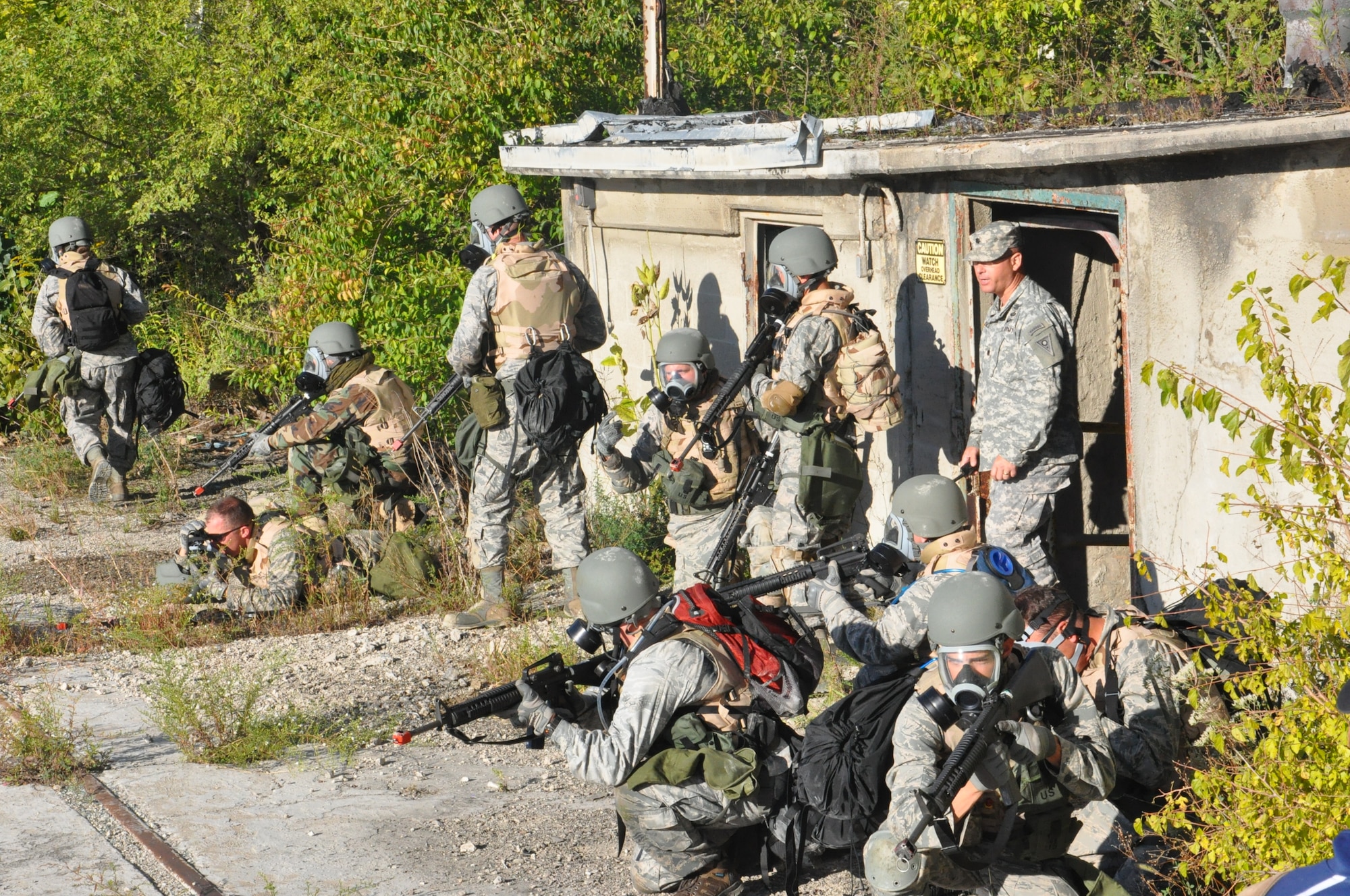 Under the watchful eyes of Army National Guard Lt. Col. James Eriksen, himself an Army Ranger, participants in the Air Force Research Laboratory 2015 Tech Warrior exercise exit an abandoned building after a smoke grenade simulating mustard gas was released during their search for a weapons cache as part of a dismounted patrol scenario, Sept. 15, 2015, at the National Center for Medical Readiness, Fairborn, Ohio. During the exercise participants learned a variety of skills such as base defense, self-aide buddy care, tactical vehicle driving and land navigation. (U.S. Air Force photo by Bryan Ripple / Released)