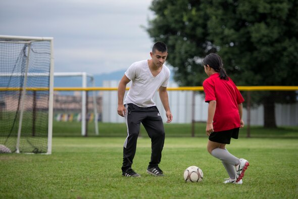 Airman 1st Class Tomasz Barba, volunteer soccer coach, practices a handling technique with a youth soccer participant at Yokota Air Base, Japan, Sept. 15, 2015. Yokota’s Youth Sports Program is extensive and relies upon hundreds of volunteers to serve as coaches, assistant coaches, and team parents. (U.S. Air Force photo by Airman 1st Class Delano Scott/Released)