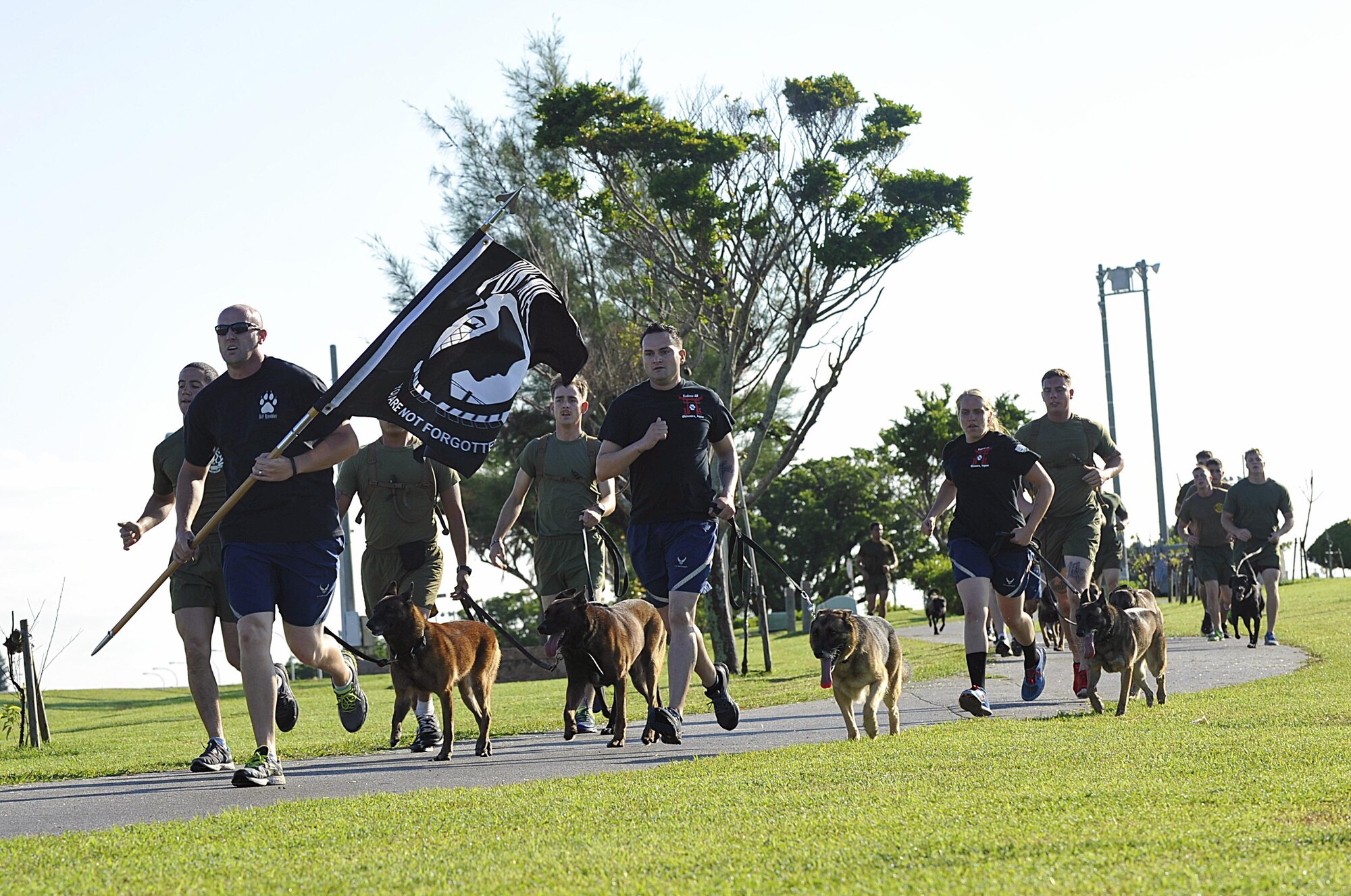 The18th Security Forces Squadron military working dog team escorts the Prisoner of War/Missing in Action flag on the first lap of the run at Marek Park Sept. 17, 2015, on Kadena Air Base, Japan. The flag will be continuously carried around the track by volunteers for the next 24 hours. Also during the run, the names of personnel who were POWs or MIAs, will be read by narrators. (U.S. Air Force photo by Naoto Anazawa/Released)
