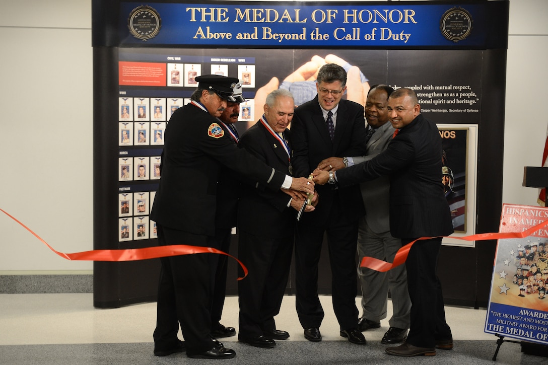 Rick Leal, president of the Hispanic Medal of Honor Society, third left, and Clarence Johnson, second from right, director of the Defense Department's Office of Diversity Management and Equal Opportunity, help cut the ribbon to open a display showcasing Hispanic Medal of Honor recipients at the Pentagon, Sept. 18, 2015.