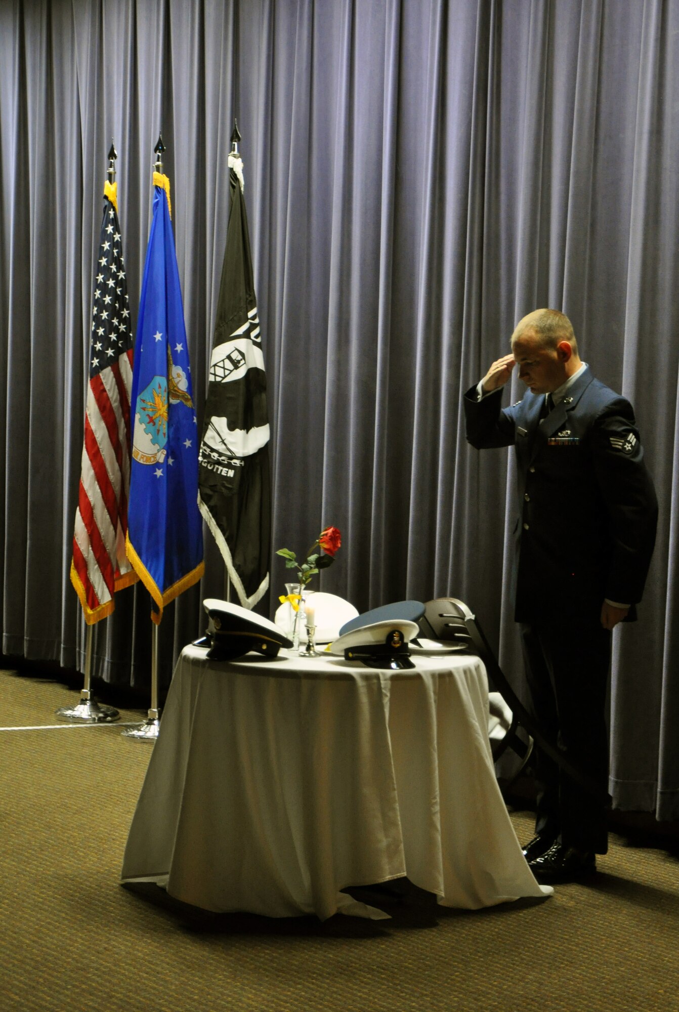 U.S. Air Force Senior Airman Mearl Ledvina, 16th Weather Squadron, salutes a table set for one Sept. 19 at the 557th Weather Wing Prisoner of War/Missing in Action Remembrance Ceremony. The table which remains unoccupied is representative of military members listed as POW/MIAs. (U.S. Air Force photo by Staff Sgt. Rachelle Blake)