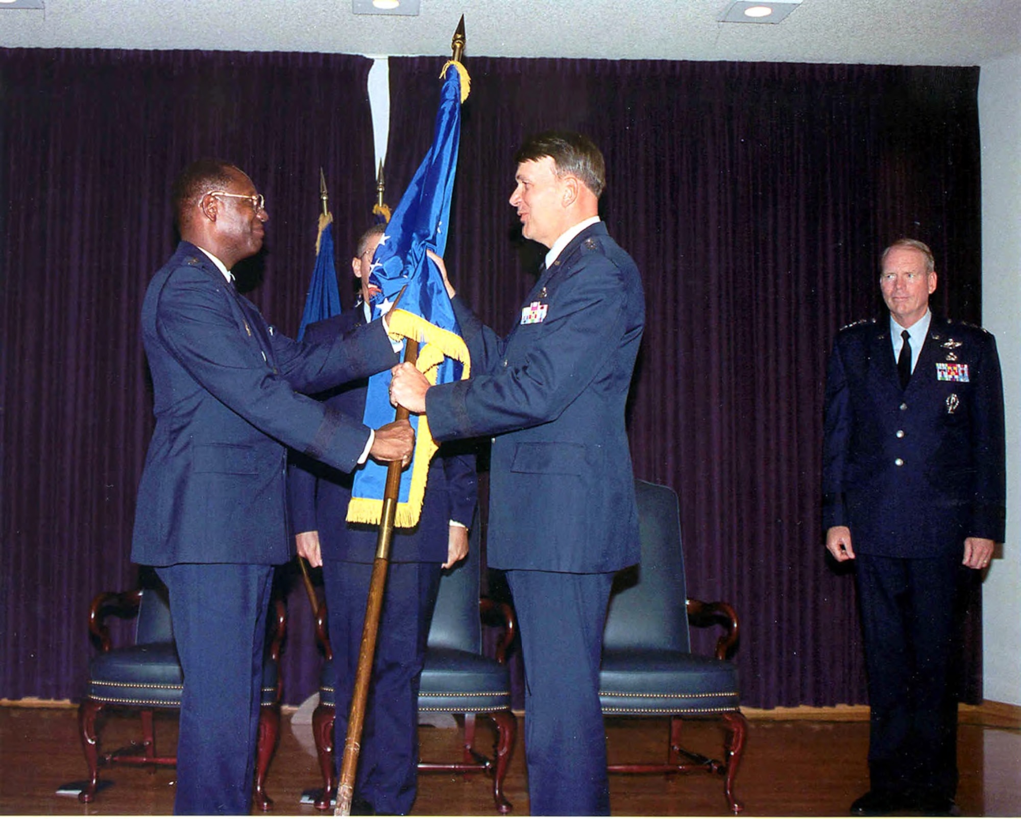 General Lester L. Lyles, commander of Air Force Materiel Command, hands SMC's flag to Lt. Gen. Roger G. DeKok, vice commander of Air Force Space Command, during ceremonies observing SMC's transfer from AFMC to AFSPC in July 1992. Lt. Gen. Brian A. Arnold, commander of SMC, stand at right. Both Lyles and DeKok were former commanders of SMC. (U.S. Air Force photo)