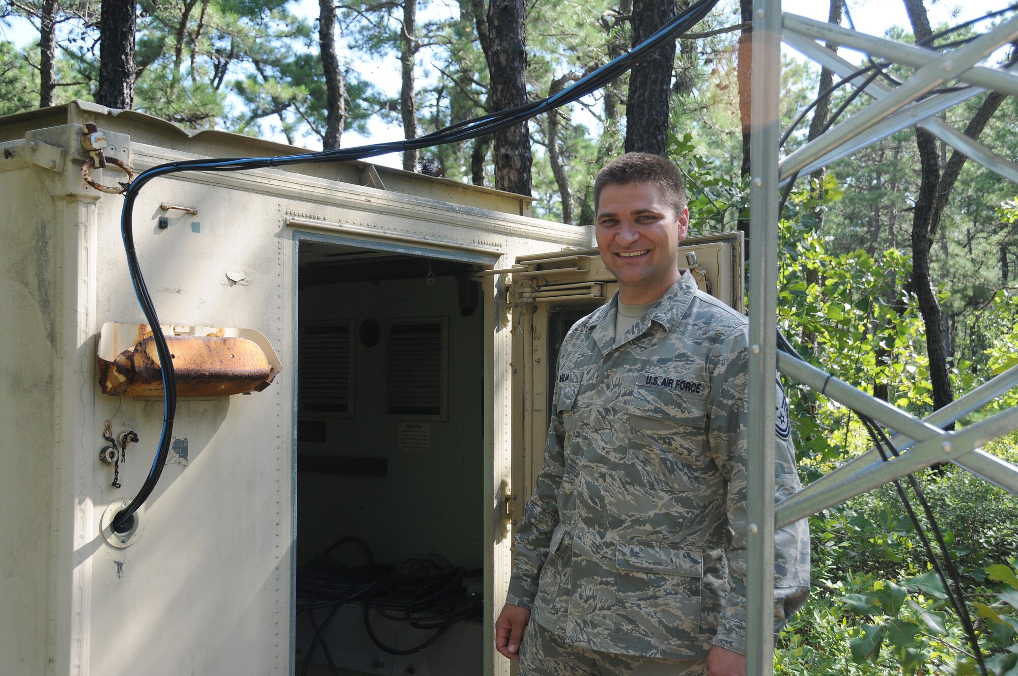 A picture of U.S. Air Force Master Sgt. Samuel Arlia standing outside of the structure of the solar charging system he created.