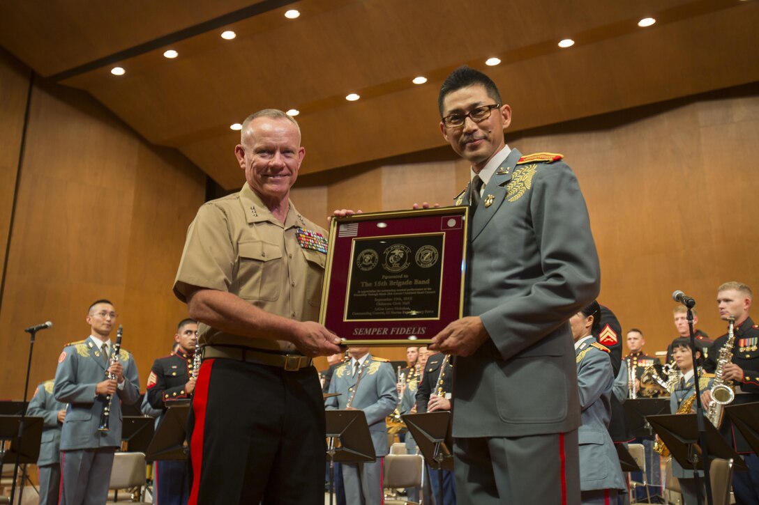 U.S. Marine Lt. Gen. Larry Nicholson, commanding general, III Marine Expeditionary Force, presents Japan Ground Self-Defense Force 1st Lt. Toshiyuki Ishimura, 15th Brigade Band director, with a plaque during the 20th Annual Combined Band Concert, at Okinawa Civic Hall, in Okinawa City, Okinawa, Japan, Sept. 19, 2015. The concert celebrated the long-standing relationship between the Marine and JGSDF musical ensembles, affording them the opportunity to once again combine forces and musically stimulate an audience.
