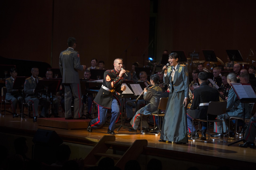 U.S. Marine Staff Sgt. Justin Schmidt and Leading Pvt. Kana Furusho with the 15th Brigade Band, Japan Ground Self-Defense Force, sing together during the 20th Annual Combined Band Concert, at Okinawa Civic Hall, in Okinawa City, Okinawa, Japan, Sept. 19, 2015. The concert celebrated the long-standing relationship between the Marine and JGSDF musical ensembles, affording them the opportunity to once again combine forces and musically stimulate an audience. Schmidt, from Wauconda, Illinois, is the small ensemble leader and a vocalist with the III Marine Expeditionary Force Band, III Marine Expeditionary Force Headquarters Group, III MEF.