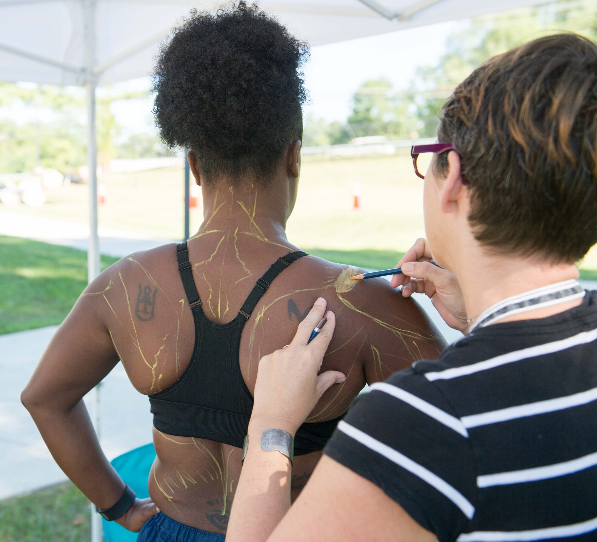Description: Anatomy of Sports at NMHM, August 2015.       Caption: Medical illustrator Alexandra Baker outlines the back and shoulder muscles of U.S. Air Force Tech. Sgt. Davita Vega during the National Museum of Health and Medicine’s annual Anatomy of Sports program, held Aug. 22, 2015, in Silver Spring, Maryland.  (Disclosure: This image has been cropped to emphasize the subject.) (National Museum of Health and Medicine photo by Matthew Breitbart/ Released)