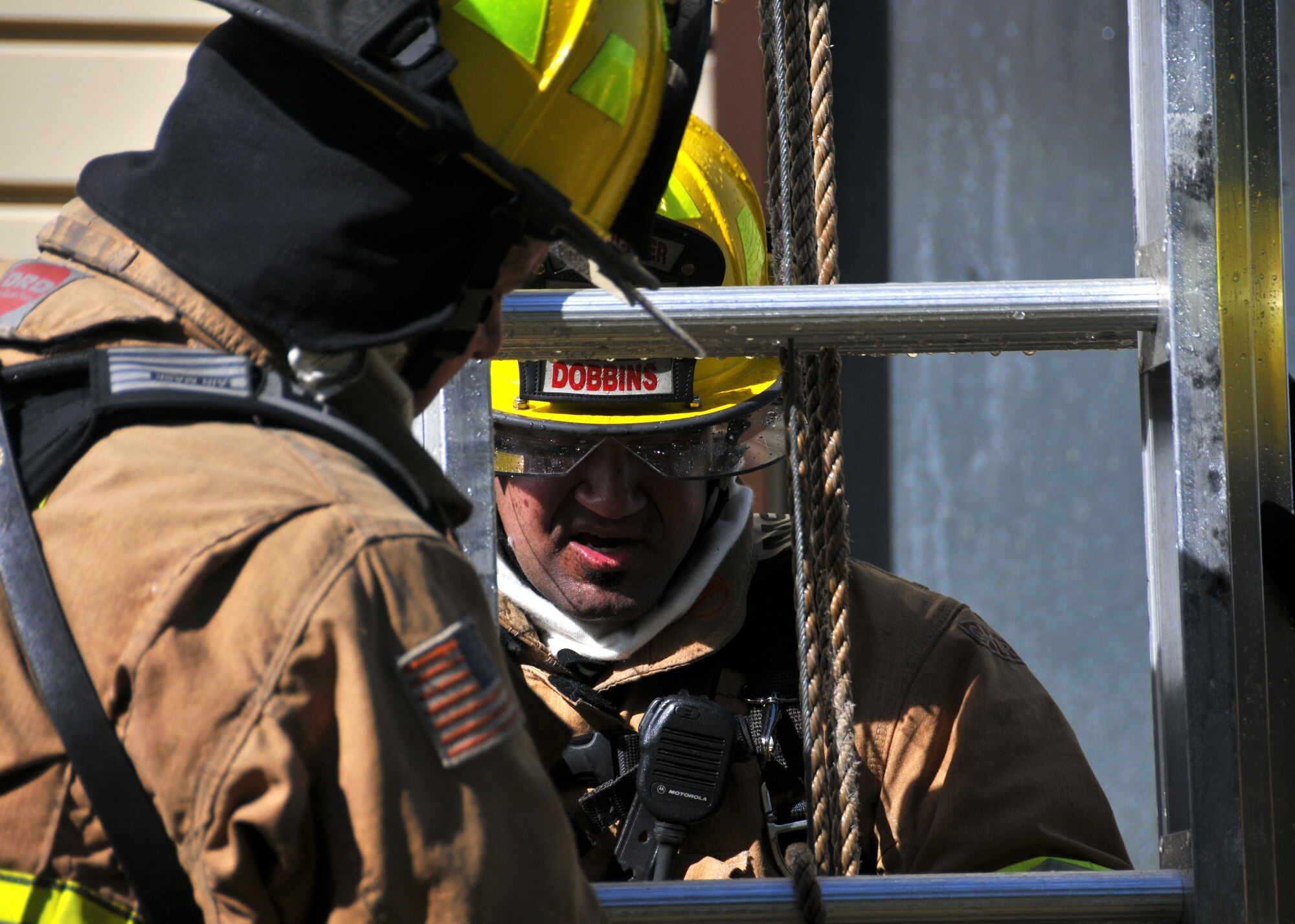 Two Dobbins firefighters secure the ladder after retrieving the training dummy from the second floor window at Dobbins Air Reserve Base, Ga. Sept. 15, 2015. Spray from a nearby hose creates slippery conditions as the firefighter ascends and descends the ladder. (U.S. Air Force photo/Senior Airman Andrew Park) 