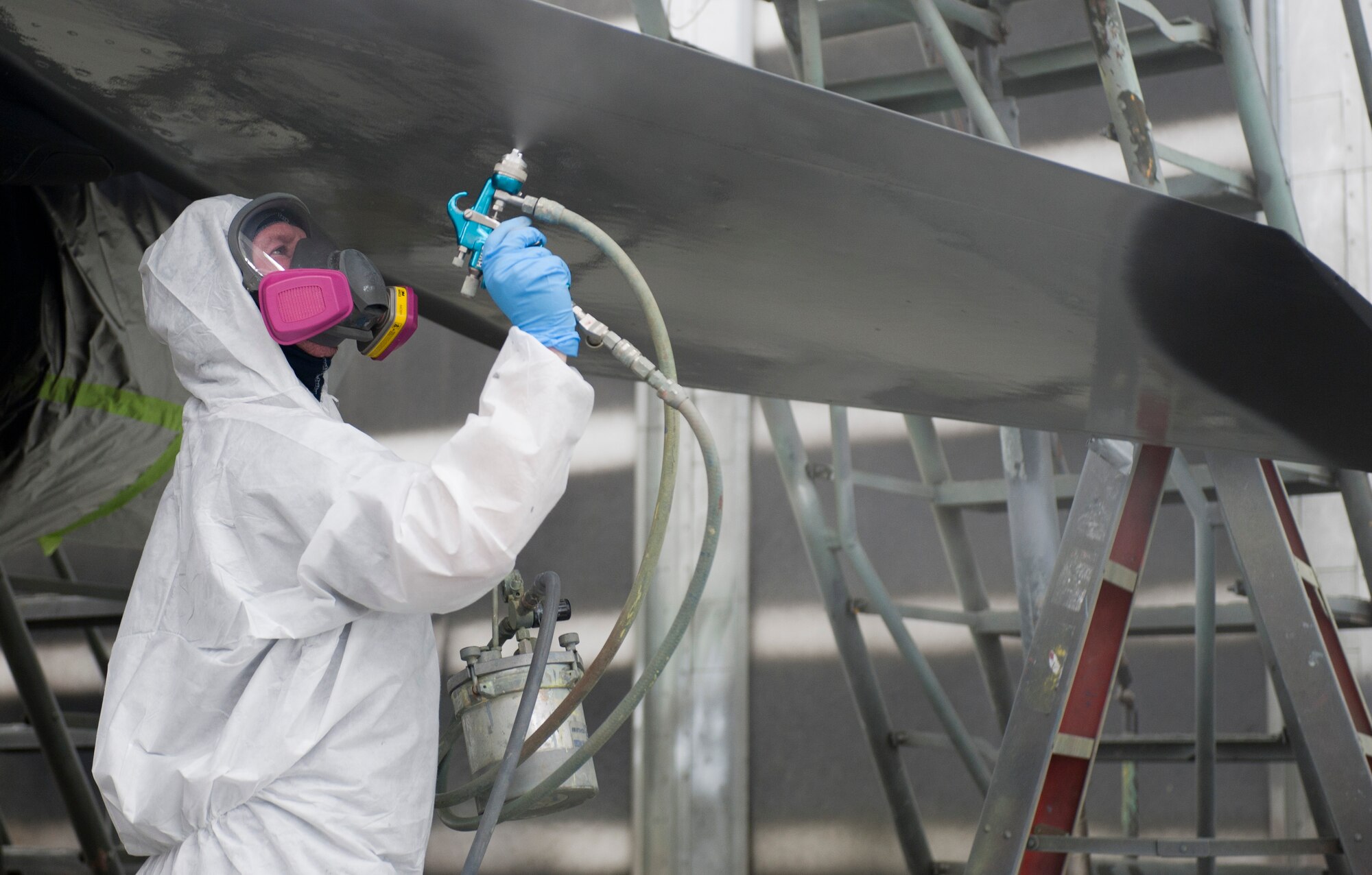 Sean Cornwall, 57th Maintenance Group Corrosion shop aircraft painter, sprays paint onto an F-16 Fighting Falcon inside a temperature-controlled building on Nellis Air Force Base, Nev., Sept. 10, 2015. The paint patterns used on aggressor aircraft are supposed to mirror one another. (U.S. Air Force photo by Airman 1st Class Mikaley Kline)