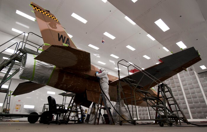 Troy Blaschko, 57th Maintenance Group Corrosion shop aircraft painter, demonstrates how to scuff sand an F-16 Fighting Falcon inside a temperature-controlled building on Nellis Air Force Base, Nev., Sept. 8, 2015. Blaschko is preparing the aircraft to undergo a full paint job. (U.S. Air Force photo by Airman 1st Class Mikaley Kline)
