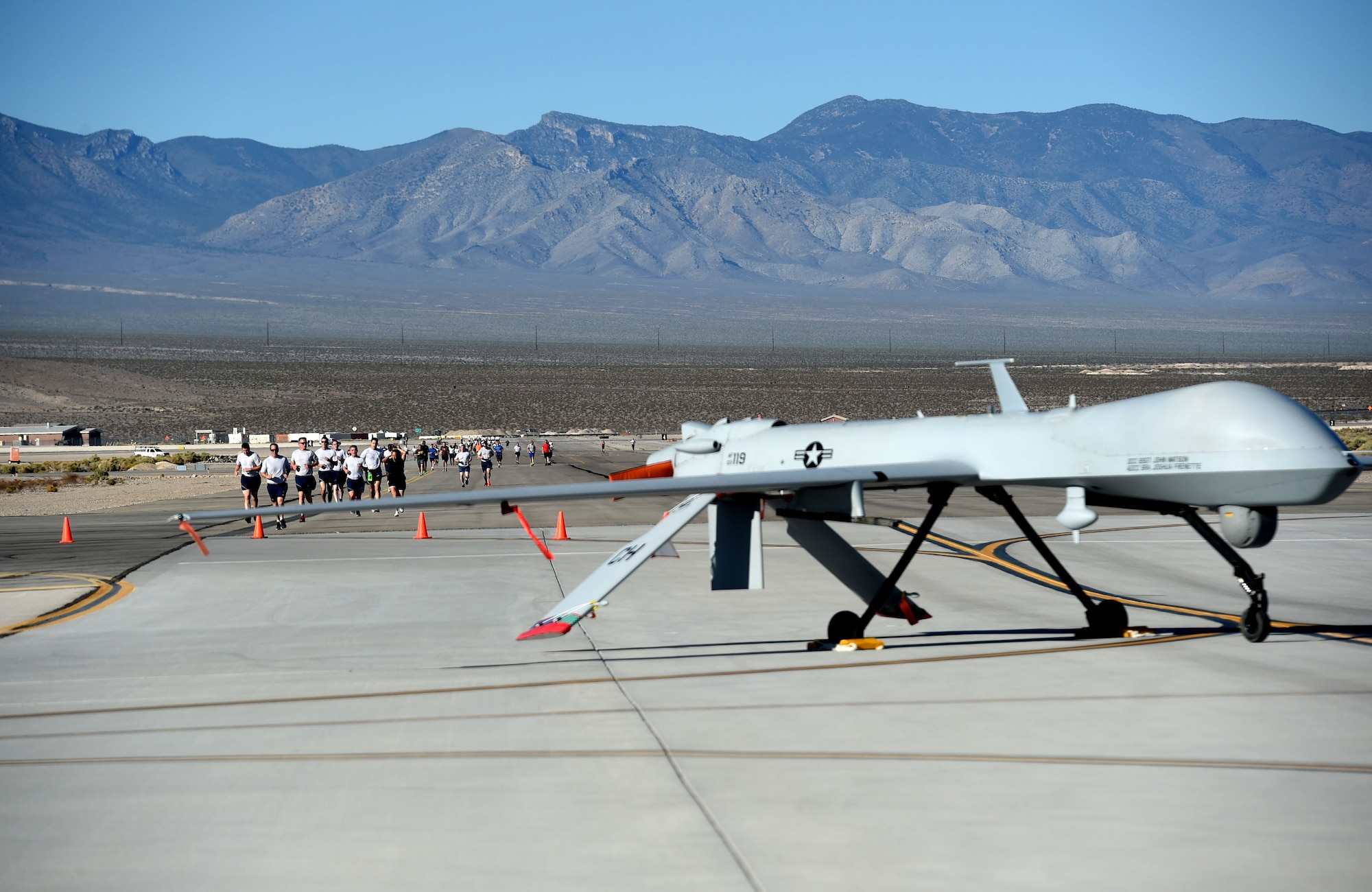 Airmen of the 432nd Wing/432nd Air Expeditionary Wing run past a MQ-1 Predator on the Creech Air Force Base, Nevada, during the 432nd Maintenance Group Golden Bolt 5K, Sept. 14, 2015. The 5K took place on the Creech flightline to raise awareness about the damages foreign object debris(FOD) can cause to aircraft on the runway. A golden bolt was placed on the course so runners were actively engaged in the collection of FOD. (U.S. Air Force photo by Tech. Sgt. Nadine Barclay)  