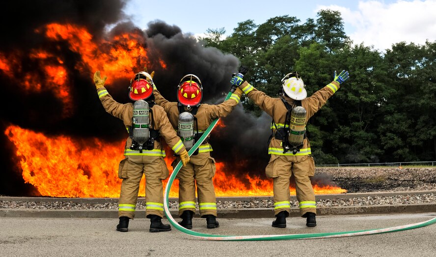 Fire protection specialists with the 182nd Civil Engineer Squadron, Illinois Air National Guard, perform their tradition of raising their hands to the jet fuel fire before extinguishing it during a controlled burn at Wingman and Family Day at the 182nd Airlift Wing, Peoria, Ill., Sept. 12, 2015. The event was organized to promote resiliency in Airmen and their friends and family. (U.S. Air National Guard photo by Staff Sgt. Lealan Buehrer/Released)