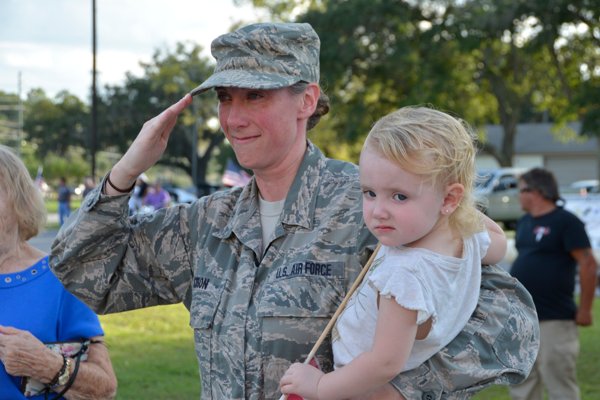 PANAMA CITY, Fla. - Master  Sgt. Tiffany Watson, Continental U.S. Aerospace Defense Region- 1st Air Force (Air Forces Northern) Chief of Staff’s Knowledge Management Office, holds her daughter Bailey as she salutes arriving wounded warriors during the Warrior Beach Retreat parade event Sept. 17. The Retreat honors wounded warriors by bringing them and their spouse or caregiver to Panama City Beach, Fla., for a week of rest and relaxation. (Air Force Photo Released/Mary McHale)
