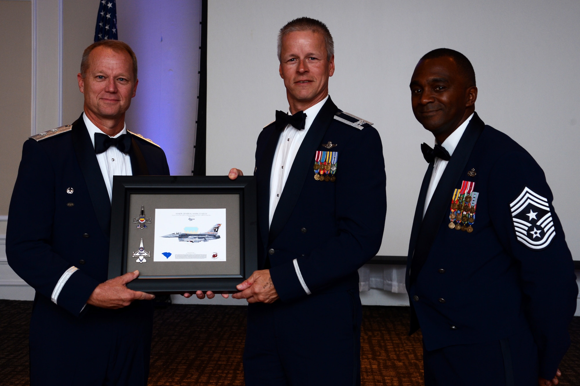 U.S. Air Force Maj. Gen. Mark Kelly, Ninth Air Force commander, receives a lithograph of an F-16CM Fighting Falcon from Col. Bill Jones, 20th Fighter Wing vice commander, and Chief Master Sgt. Christopher McKinney, 20th FW command chief, during the Shaw Air Force Ball at Shaw Air Force Base, S.C., Sept. 18, 2015. Kelly, the guest speaker, is a command pilot with more than 5,500 hours flying the T-37 Tweet, T-38 Talon, F/A-18 Super Hornet, F-15 Eagle, and F-16 Fighting Falcon. (U.S. Air Force photo by Senior Airman Jonathan Bass/Released)