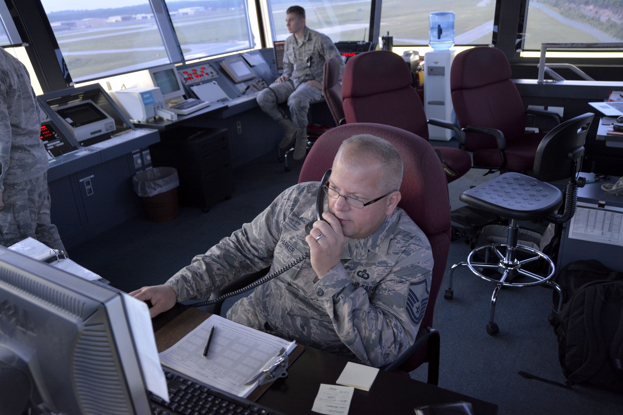 235th Air Traffic Control Squadron, Tower Watch Supervisor, Master Sgt. Tony L. Parker, makes entries in the daily event log as Senior Airman James D. Bellissimo, ground controller; surveys taxi ways at Stanly County Airport, New London, N.C., July 8, 2015. The 235th ATCs provides air traffic control services for all civilian and military aircraft at the Stanly County Airport, New London, N.C. (U.S. Air National Guard photo by Master Sgt. Patricia F. Moran, 145th Public Affairs/Released) 