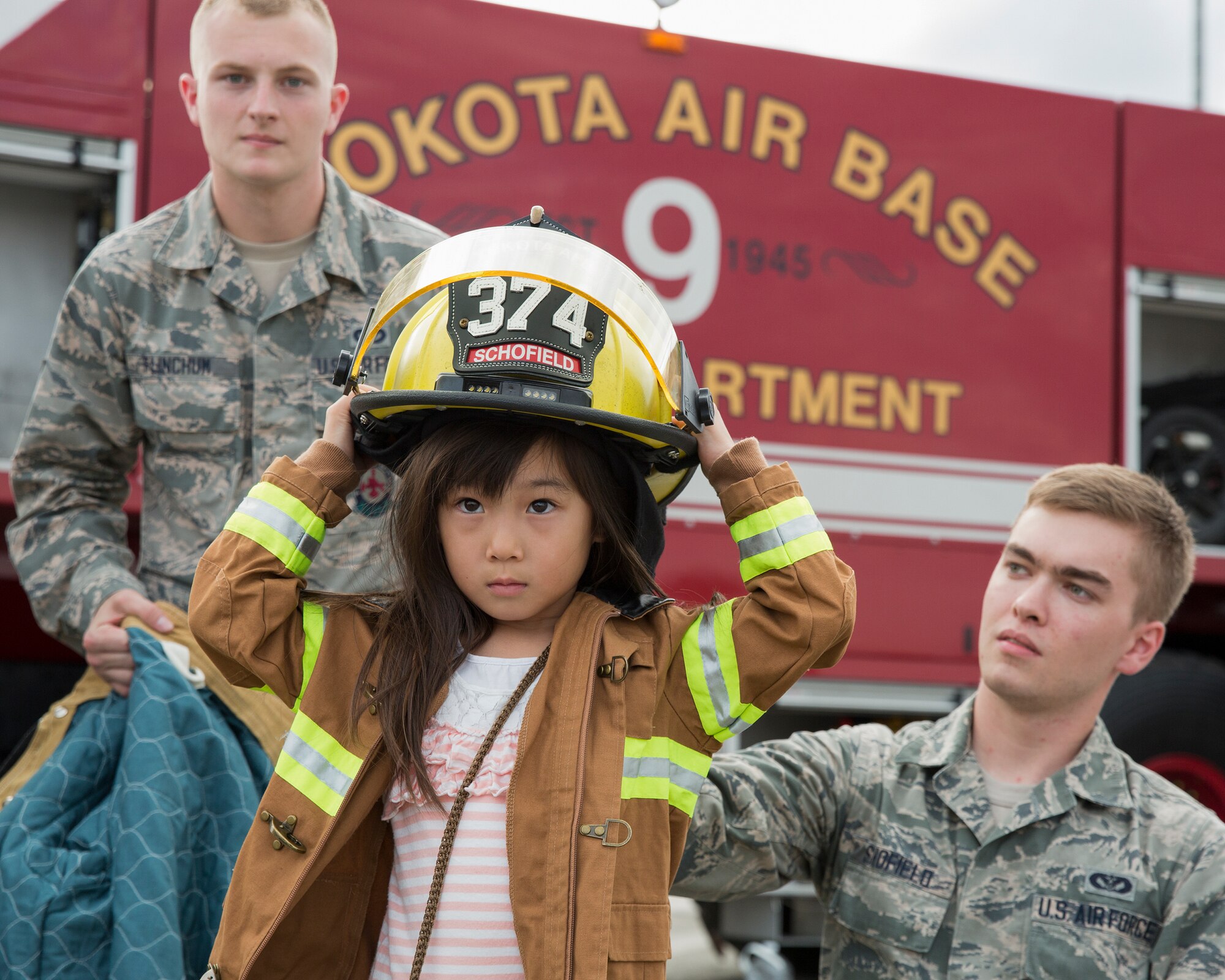 (Right to left) Airman 1st Class Zachary Schofield and Airman Luke Flinchum, both 374th Civil Engineer Squadron firefighters, help a local girl put on a firefighting suit for a portrait at Yokota Air Base, Japan, during the Japanese-American Friendship Festival Sept. 19, 2015. Yokota welcomed 185,000 visitors during the two-day festival. (U.S. Air Force photo by Osakabe Yasuo/Released) 