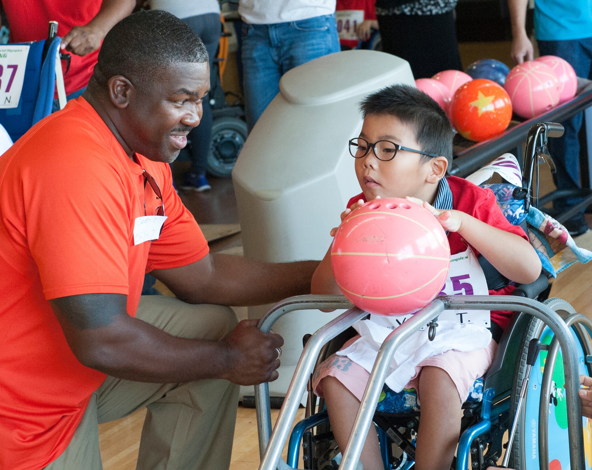 U.S. Air Force Master Sgt. Cedric Smith, 18th Equipment Maintenance Squadron aerospace ground equipment production superintendent, helps Yuko, Kadena Special Olympics athlete, push the ball off of the ramp during the KSO bowling event at Enagic Bowling in Mihama, Japan, Sept. 19, 2015. Athletes shared the lane with two others as they took turns to bowl two games. (U.S. Air Force photo by Airman 1st Class Corey M. Pettis)