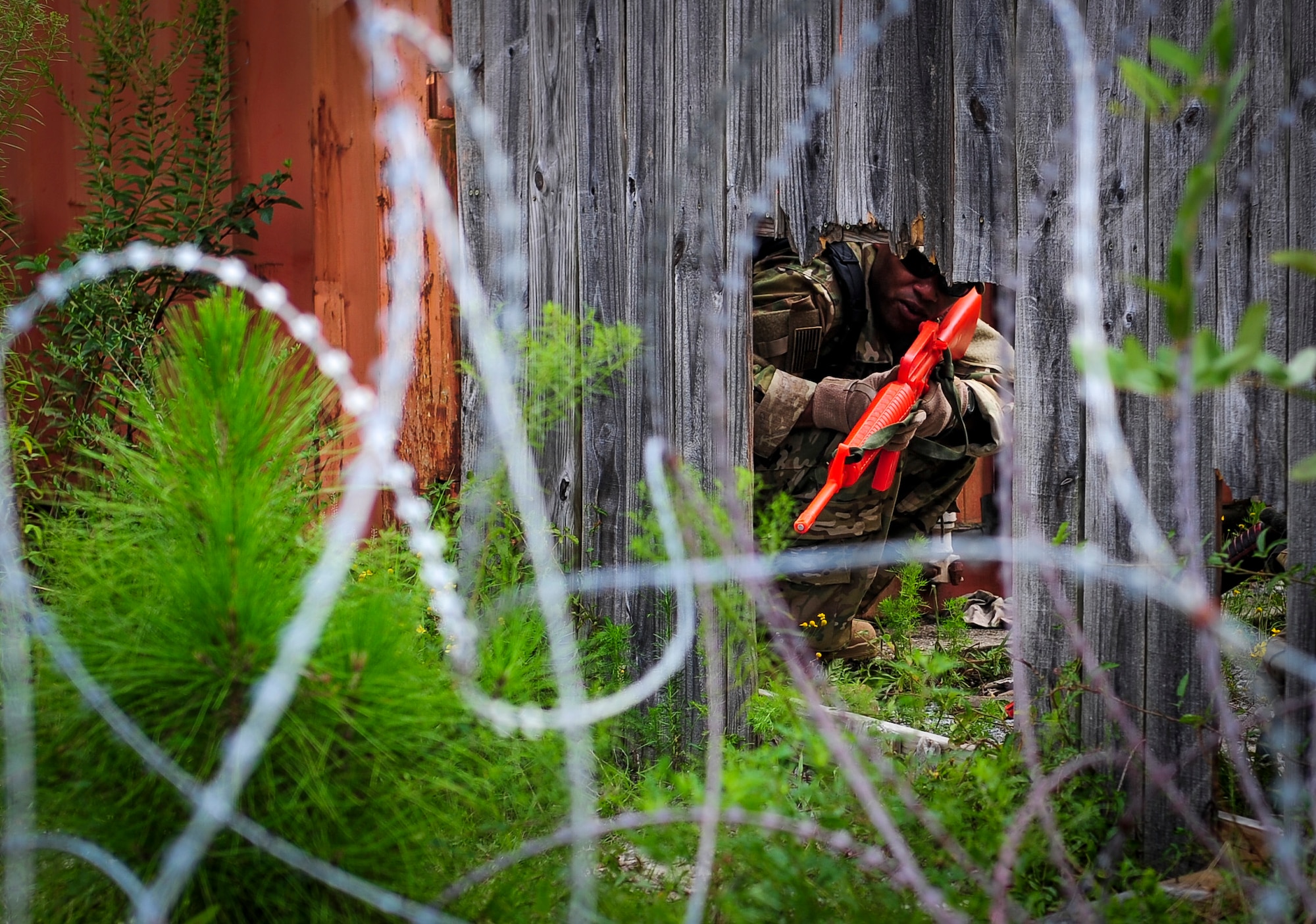 Staff Sgt. Brandon Waithe, 25th Intelligence Squadron tactical systems operator, peers through a fence during urban clearing training at Eglin Field Complex, Fla., Sept. 2, 2015. Aircrew members participate in combat survival training tri-annually to maintain proficiency on skill sets such as combative, evasion, navigation, signaling, radio use and discipline and contact procedures. (U.S. Air Force photo by Senior Airman Meagan Schutter)