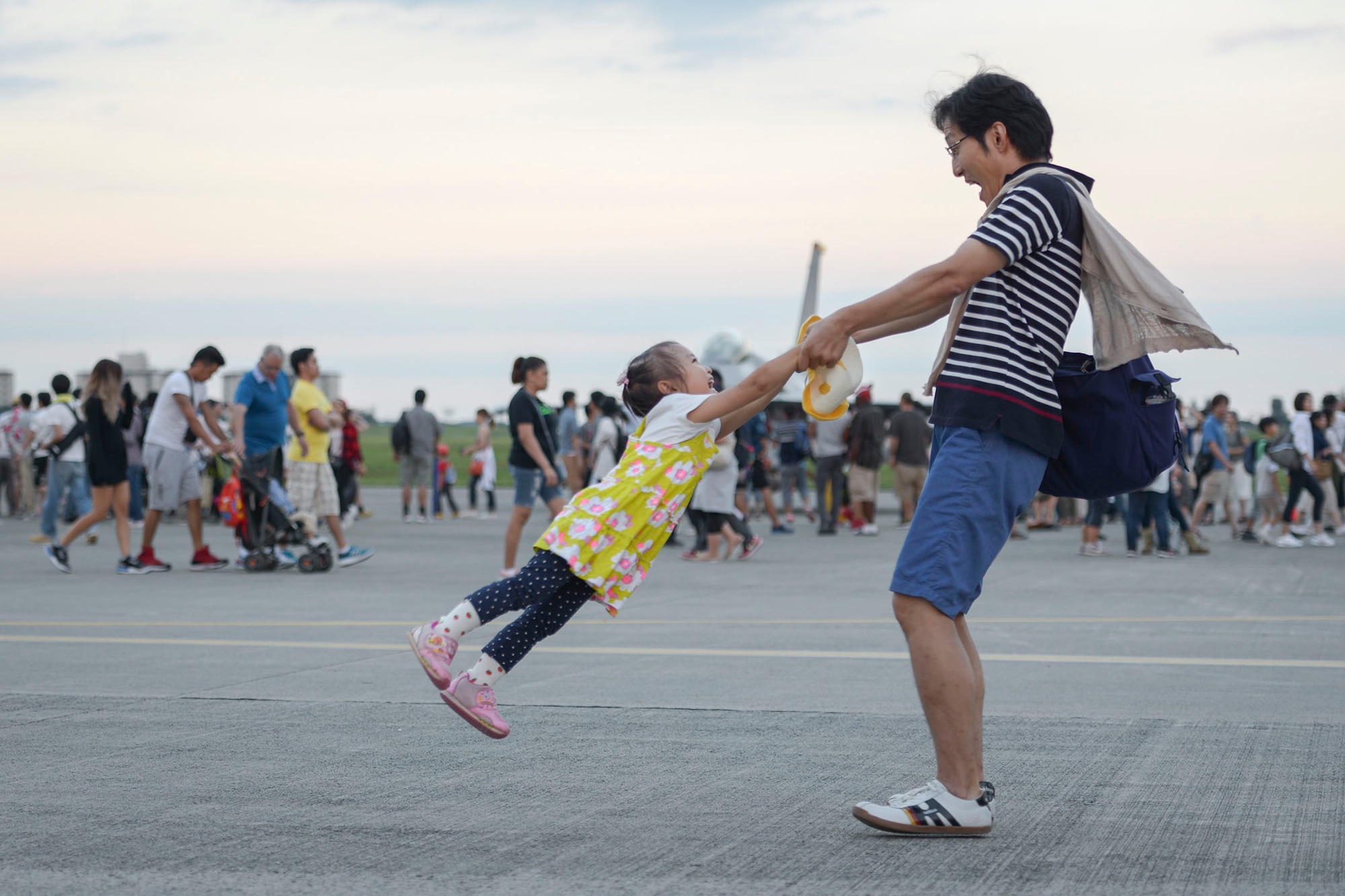 A father swings her daughter in front of aircraft static displays during the 2015 Japanese-American Friendship Festival at Yokota Air Base, Japan, Sept. 20, 2015. The festival had 28 aircraft on display, allowing participants to see inside each aircraft, sit in the cockpits, greet the aircrew and take photos. (U.S. Air Force photo by Staff Sgt. Cody H. Ramirez/Released)