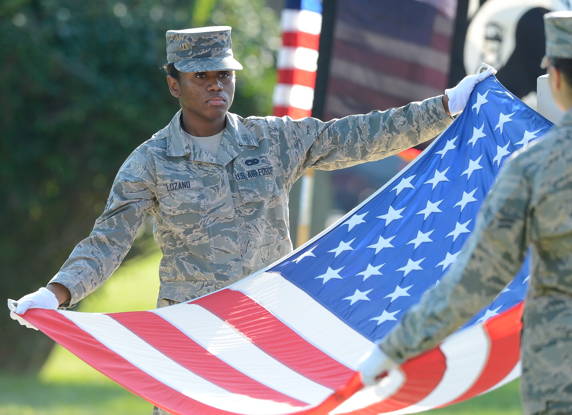 Airman 1st Class Monique Lozano, 436th Aerial Port Squadron, left, and A1C Alaina Marti, 436th Logistics Readiness Squadron, extend their arms to reveal the colors of the American flag before folding it during the National POW/MIA Recognition Day on Sept. 18, 2015, on Dover AFB, Del. Team Dover conducted a run, vigil at the base flagpole and a formal retreat ceremony. (U.S. Air Force photo/Greg L. Davis)
