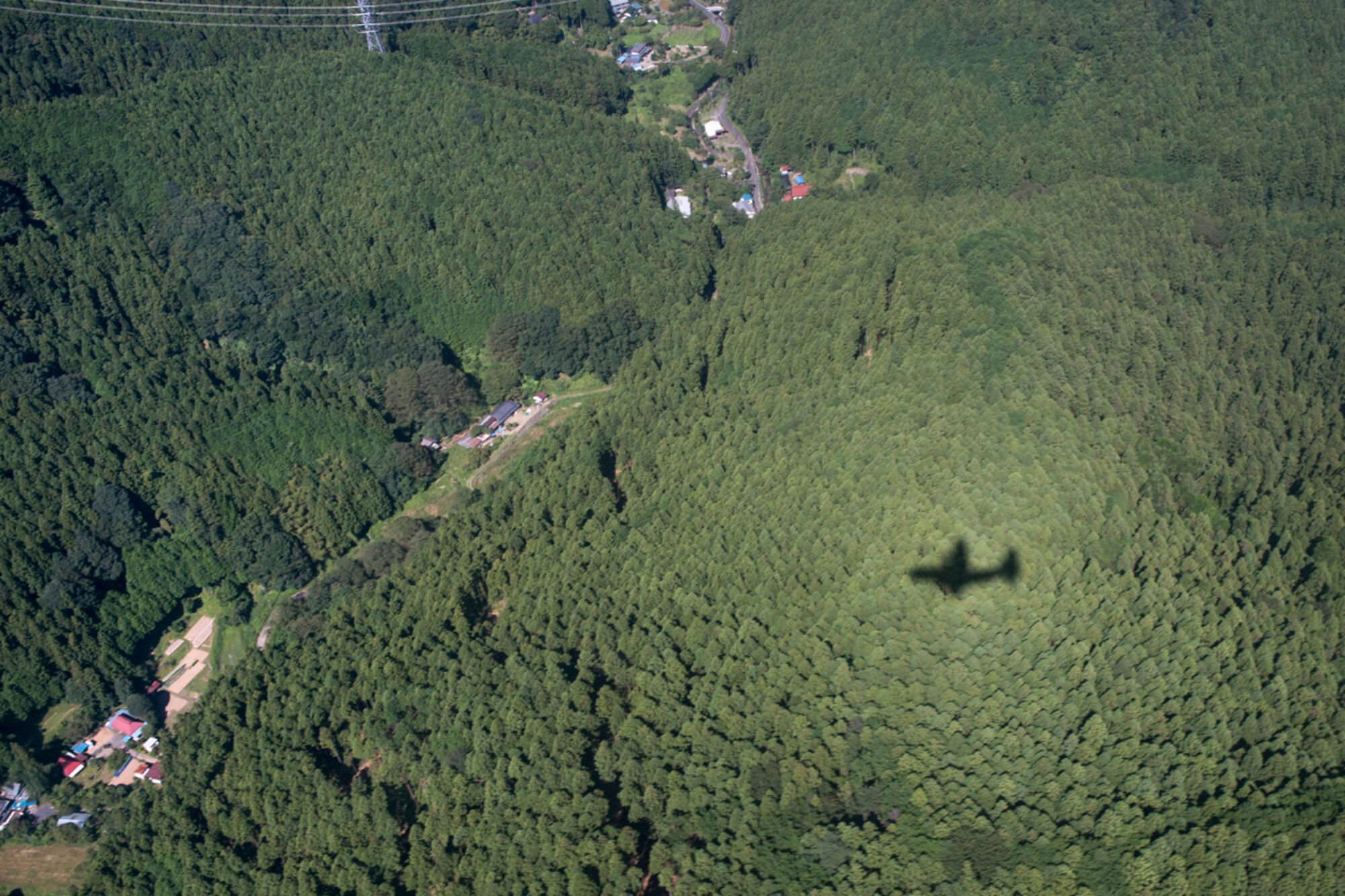 A shadow of a C-130 Hercules darts through trees before an airdrop demonstration during the 2015 Japanese-American Friendship Festival at Yokota Air Base, Japan, Sept. 19, 2015. The Hercules dropped more than 40 Soldiers with the  1st Battalion, 1st Special Operations Group (Airborne), during the two-day festival to showcase the airdrop capability at Yokota. (U.S. Air Force photo by Staff Sgt. Cody H. Ramirez/ Released)