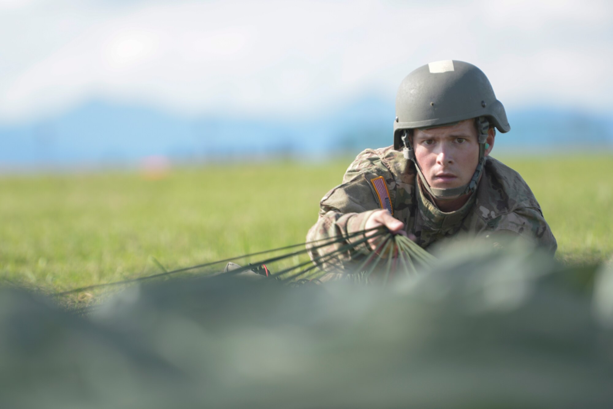 A Soldier with the 1st Battalion, 1st Special Operations Group (Airborne), pulls in his parachute while laying prone during the 2015 Japanese-American Friendship Festival at Yokota Air Base, Japan, Sept. 19, 2015. The jump displayed Yokota's airdrop capability to the festival attendees while also allowing the Airborne members to receive scheduled training and update jump currency. (U.S. Air Force photo by Staff Sgt. Cody H. Ramirez/ Released)