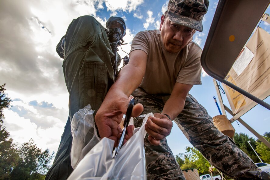 Staff Sgt. Miguel A. Berroa, Aircrew Flight Equipment, 108th Wing, New Jersey Air National Guard, cuts off Airman 1st Class Justin Addison’s plastic booties – part of the aircrew eye and respiratory protection system – during aircrew contamination control area training at Joint Base McGuire-Dix-Lakehurst, N.J., Sept. 19, 2015. The ACCA decontamination process is a series of stations with signs showing detailed instructions on how to decontaminate aircrew members. Aircrew Flight Equipment Airmen instruct the Wing’s KC-135R Stratotanker crew members on the proper use of the aircrew eye and respiratory protection system – part of the aircrew chemical, biological, radiological and nuclear equipment and are also responsible for setting up the aircrew contamination control area and decontaminating aircrew members. (U.S. Air National Guard photo by Master Sgt. Mark C. Olsen/Released)