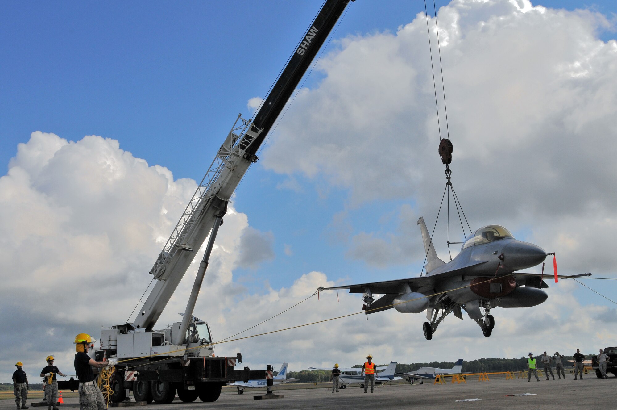 U.S. Air Force airmen from the New Jersey Air National Guard 177th Fighter Wing Crash Disabled Damaged Aircraft Recovery team maneuvering an F-16 Fighting Falcon hooked up to a crane.