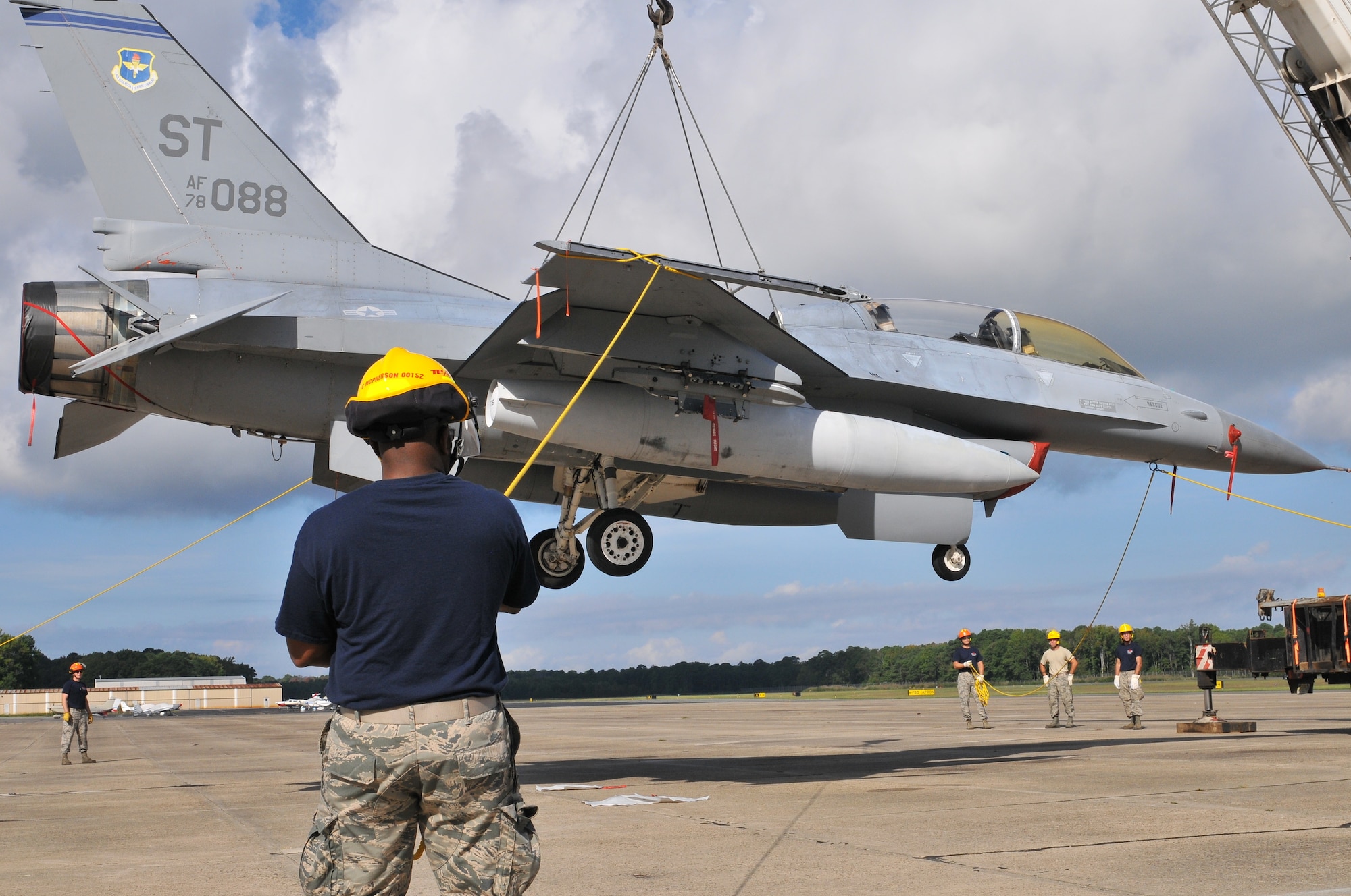 U.S. Air Force airmen from the New Jersey Air National Guard 177th Fighter Wing Crash Disabled Damaged Aircraft Recovery team maneuvering an F-16 Fighting Falcon hooked up to a crane lift.