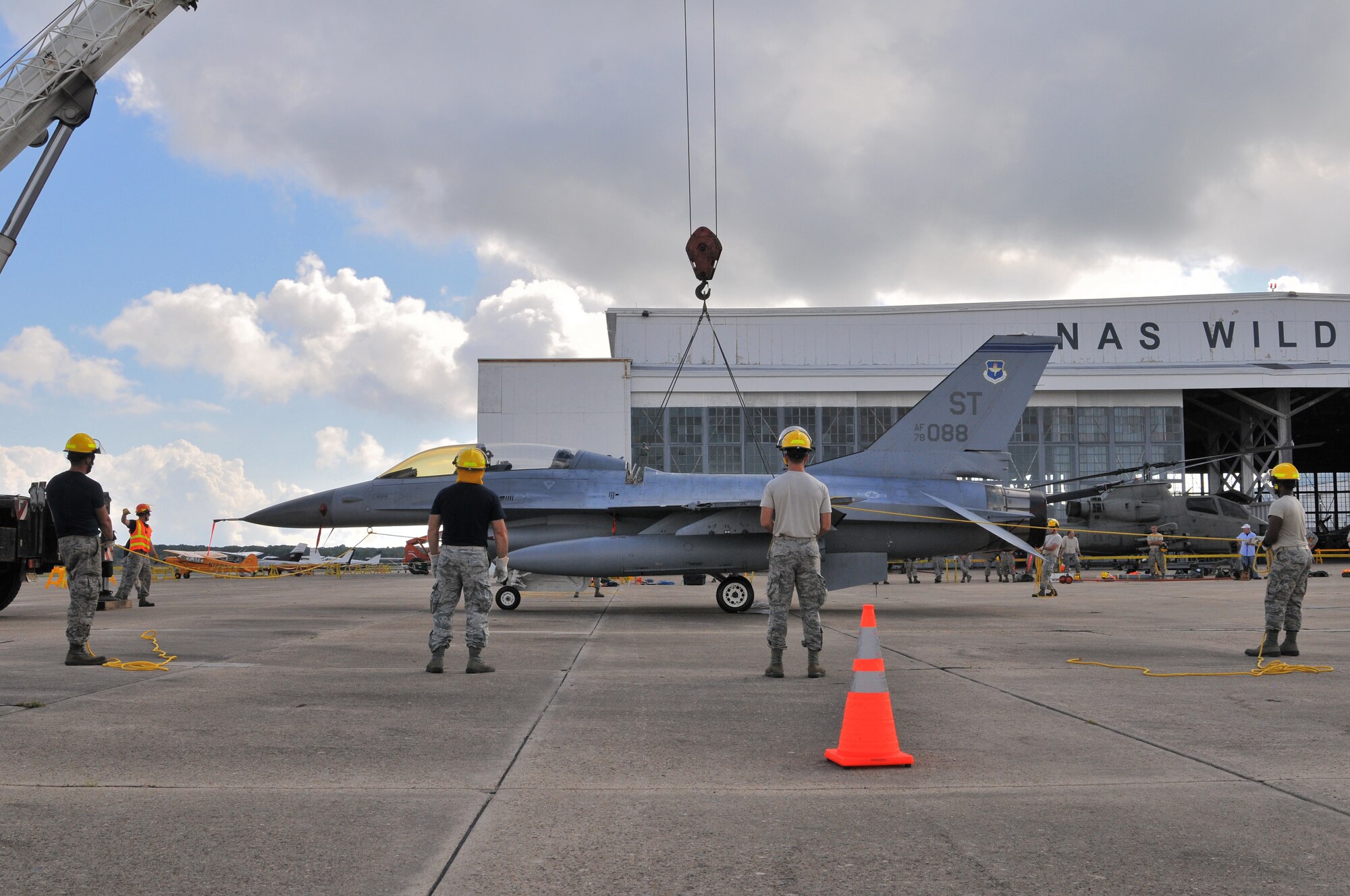 A picture of U.S. Air Force airmen from the New Jersey Air National Guard 177th Fighter Wing Crash Disabled Damaged Aircraft Recovery team maneuvering an F-16 Fighting Falcon hooked up to a crane lift.