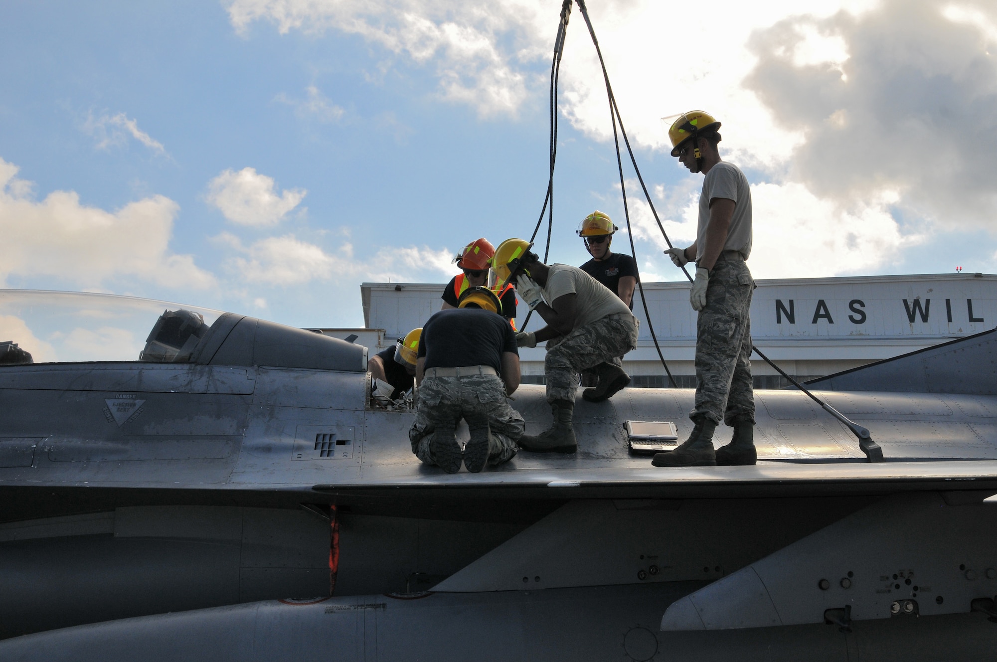 A picture of U.S. Air Force airmen from the New Jersey Air National Guard 177th Fighter Wing Crash Disabled Damaged Aircraft Recovery team working to hook a crane to an F-16 Fighting Falcon fuselage.