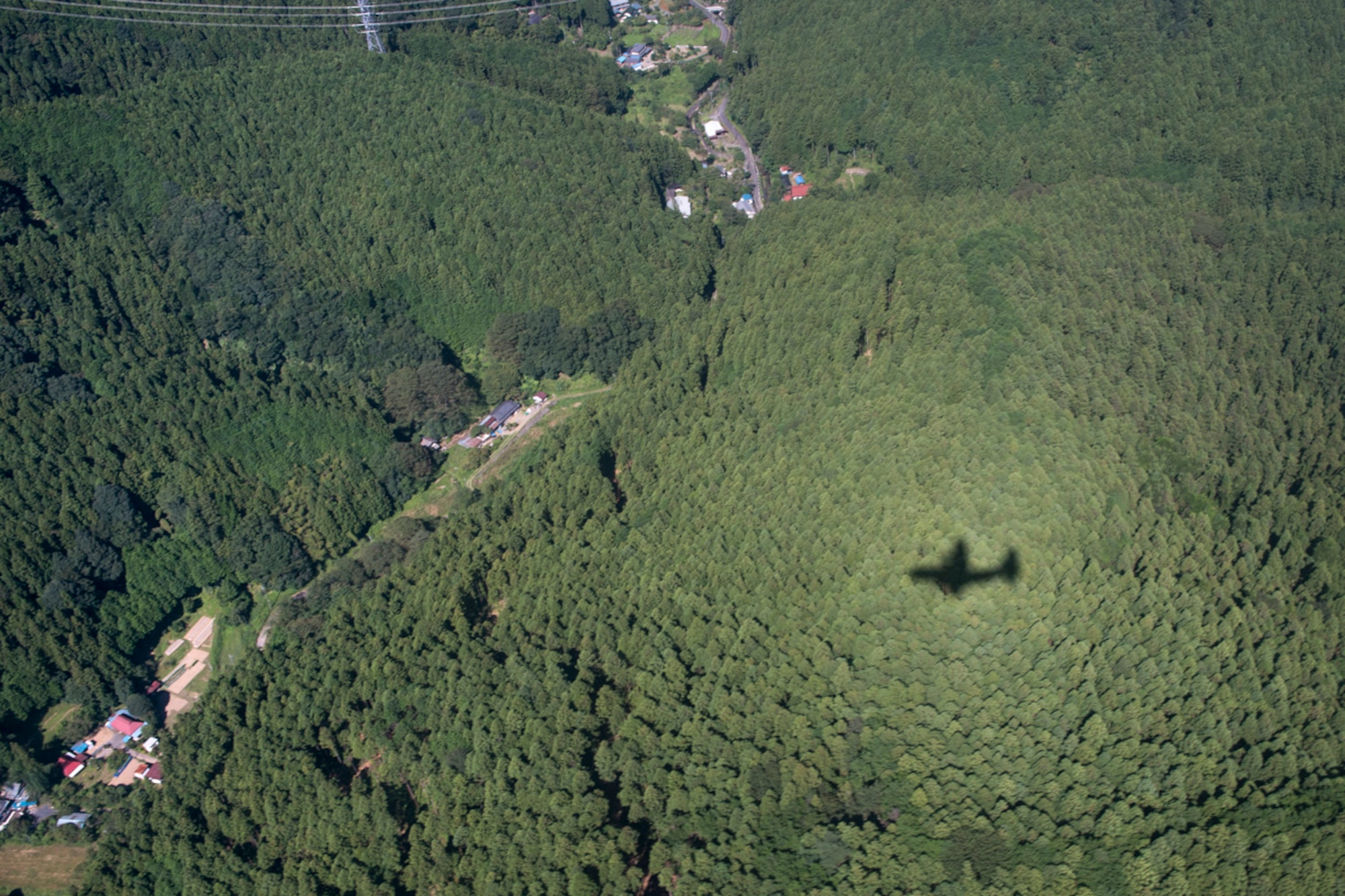 A shadow of a C-130 Hercules darts through trees before an airdrop demonstration during the 2015 Japanese-American Friendship Festival at Yokota Air Base, Japan, Sept. 19, 2015. The Hercules dropped more than 40 Soldiers with the 1st Battalion, 1st Special Operations Group (Airborne), during the two-day festival to showcase the airdrop capability at Yokota. (U.S. Air Force photo by Staff Sgt. Cody H. Ramirez/ Released)