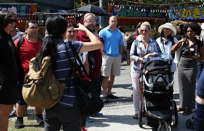 Mikie Watanabe, cultural adaption specialist with the cultural adaption program, speaks to Marine Corps Air Station Iwakuni, Japan, residents during a trip to the annual Japanese Calligraphy Brush Festival, in Kumano, Hiroshima Prefecture, Sept. 23, 2015. Guests wandered through the brush decorated city, where they interacted with Japanese locals, practiced their calligraphy skills and enjoyed local cuisine. The cultural adaption program aboard station coordinated this event to provide service members and their families a chance to travel beyond the installations gates and experience the Japanese culture.
