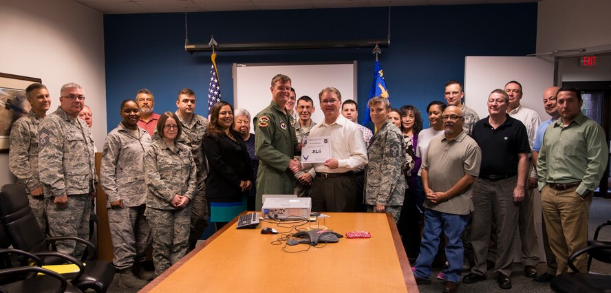 Kurt Armbruster, center, 47th Contracting Flight contracting specialist, poses with Col. Thomas Shank, 47th Flying Training Wing commander, Chief Master Sgt. Teresa Clapper, 47th FTW command chief, after accepting the “XLer of the Week” award, here, Sep. 23, 2015. The “XLer” is a weekly award chosen by wing leadership and is presented to those who consistently make outstanding contributions to their unit and Laughlin. (U.S. Air Force photo by Airman 1st Class Ariel D. Partlow) (Released)