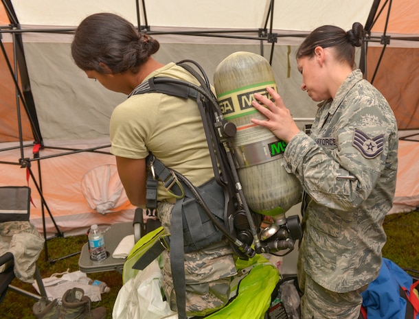 (From left to right) Airman 1st Class Vanessa Ramos, 628th Civil Engineering Squadron emergency management operator, is assisted in putting on her oxygen tank by SSgt. Jennifer Greene, 628th CES EM operator. Ramos and Greene took part in the hazardous material exercise on Joint Base Charleston – Air Base, S.C., Sept. 25, 2015. Ramos worked alongside with SrA Brandon Lane, 628th Medical Group bio-environmental technician, during the exercise. (U.S. Air Force photo/Airman 1st Class Thomas T. Charlton)