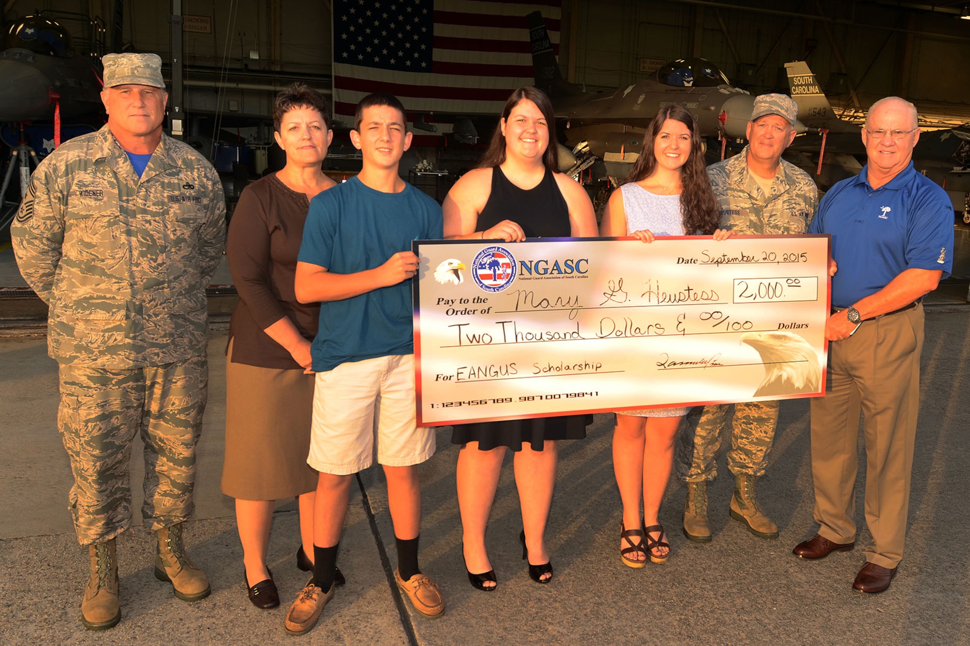 Mary Grace Heustess (third from right), daughter of U.S. Air Force Senior Master Sgt. Bo Heustess (second from right), from the South Carolina Air National Guard's 169th Aircraft Maintence Squadron's Weapons Section, receives a $2,000 scholarship check from Chief Master Sgt. (ret.) Lawrence Crowson (far right), executive director for the National Guard Association of South Carolina, and from Chief Master Sgt. Dean Widener, S.C. State Command Chief, during a unit formation at McEntire Joint National Guard Base, S.C. Sept. 20, 2015. (U.S. Air National Guard photo by Senior Master Sgt. Edward Snyder/Released)