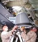 Marines muscle the Hatch-Mounted Satellite Communication Antenna System into the hatch of a C-130 Hercules aircraft. HMSAS provides secure voice, tactical classified network access, common tactical picture, secure chat and streaming intelligence and reconnaissance video for commanders in the field. 