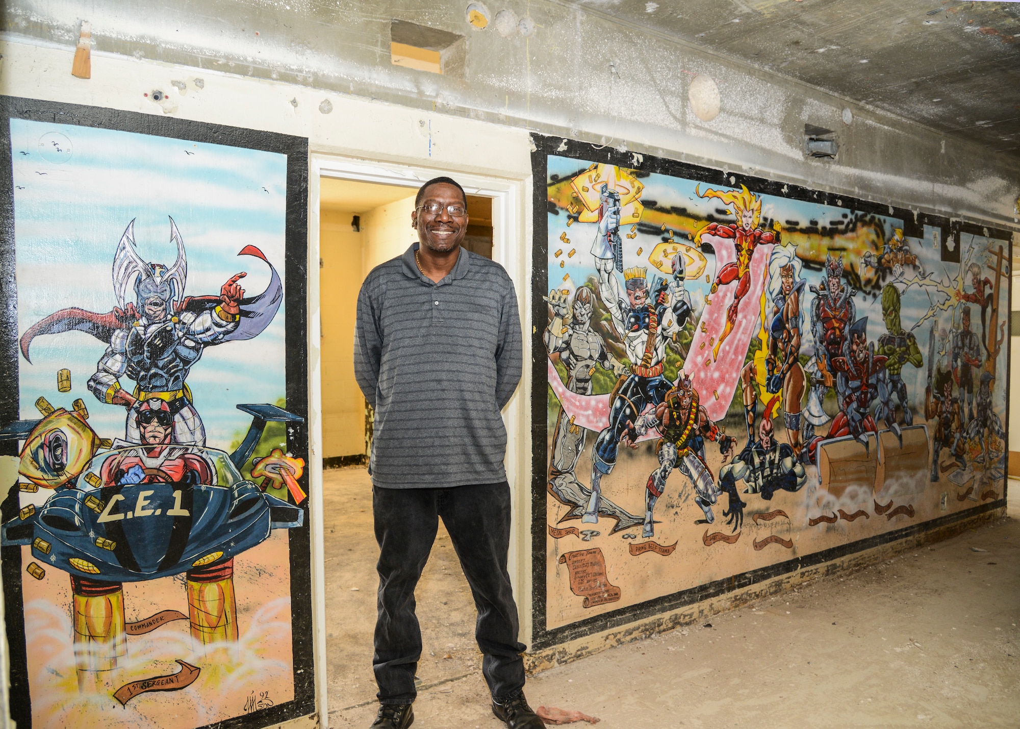 Local artist Gregory Wilson is pictured in Dorm 2424 in front of the comic book style mural he painted in 1992. The mural was uncovered several weeks ago during renovations to the building. (U.S. Air Force photo by Rebecca Amber)