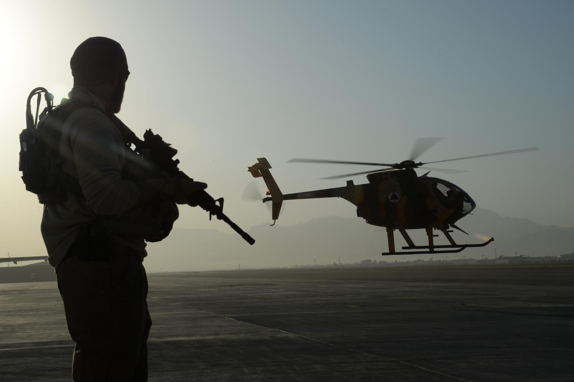 A U.S. Army Train, Advise, Assist Command – Air (TAAC-Air) personal security detail shift lead, provides security while an MD-530 Cayuse Warrior, or “Jengi” in Dari, takes off with an all-Afghan combat mission Sept. 27, 2015.  The crews flew out of Hamid Karzai International Airport, Kabul, Afghanistan. The “Jengi” is a light-lift, highly maneuverable attack helicopter used for high altitude operations. (U.S. Air Force photo by Staff Sgt. Sandra Welch/released)
