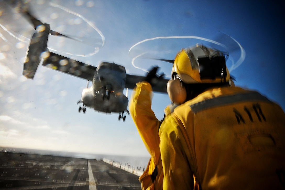U.S. Navy Petty Officer 3rd Class Donnell Jackson assists Petty Officer 1st Class Jake Kochel as Kochel signals an MV-22 Osprey for takeoff from the USS New Orleans in the Pacific Ocean, Sept. 26, 2015. The New Orleans is underway conducting training for an upcoming deployment. U.S. Navy photo by Petty Officer 1st Class Gary Granger Jr.