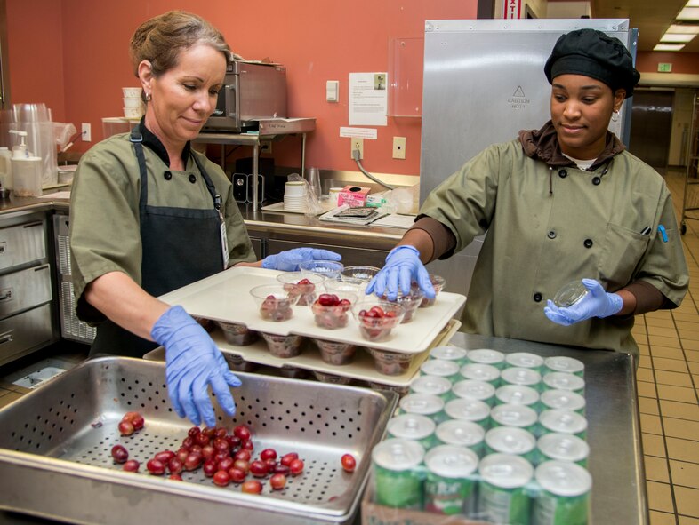 Deborah Souza (left) and Camara Ashe, 60th Diagnostics and Therapeutic Squadron nutritional medicine flight food service diet technicians, prepare cups of grapes to be distributed to the inpatients at David Grant USAF Medical Center Sept. 15, 2015. Starting Oct. 1, the dining facility will no longer be open for dinner and the breakfast and lunch hours will be shortened by 30 minutes. Breakfast will now be 6 a.m. to 8 a.m. and lunch will be 11 a.m. to 1 p.m. Starting in November, the diet technicians will have more personable, one-on-one care with the patients, providing room service for their meals. (U.S. Air Force photo/Senior Airman Nicole Leidholm)