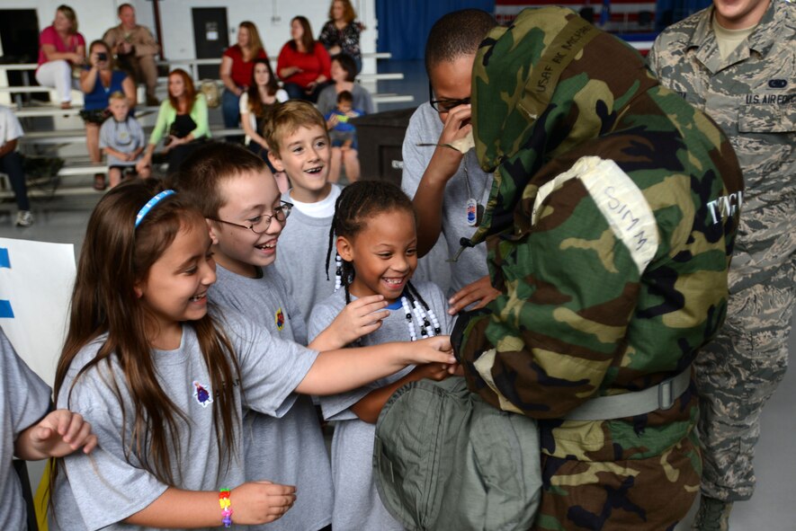 Team Shaw children assist an Airman as she dons her Mission Oriented Protective Posture gear during the Kids Meet the Viper event at Shaw Air Force Base, S.C., Sept. 23, 2015. Two Airmen raced against each other to put on the MOPP gear as the children cheered them on. (U.S. Air Force photo by Airman 1st Class Kelsey Tucker/Released)