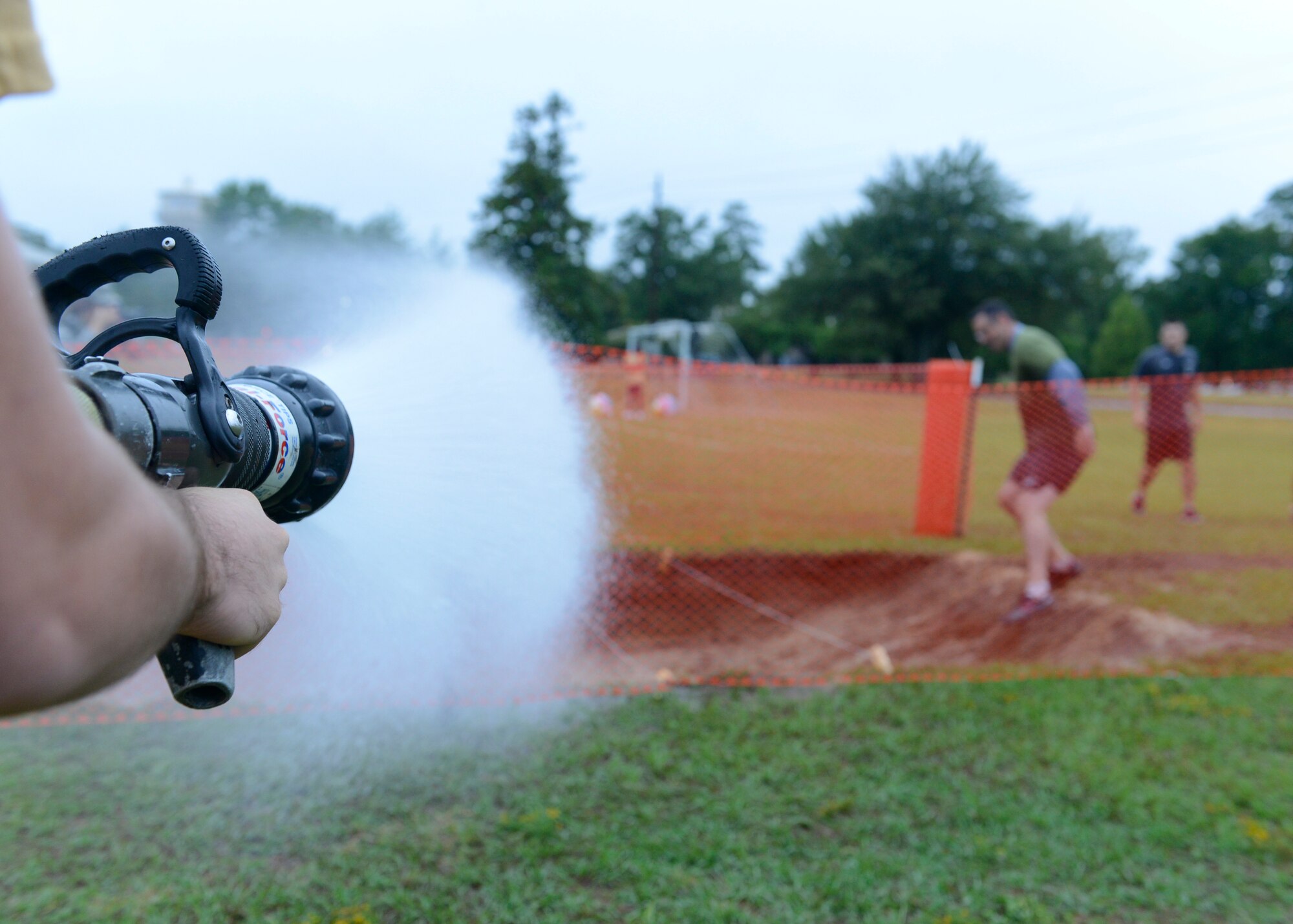 An Airman assigned to the 20th Civil Engineer Squadron fire department uses a fire hose to spray Airmen participating in a 20th Fighter Wing Comprehensive Airman Fitness week obstacle course at Shaw Air Force Base, S.C., Sept 25, 2015. Airmen had to overcome changing course conditions throughout the event, from watered-down terrain to airborne projectiles in the form of water balloons. (U.S. Air Force photo by Airman 1st Class Christopher Maldonado/Released) 