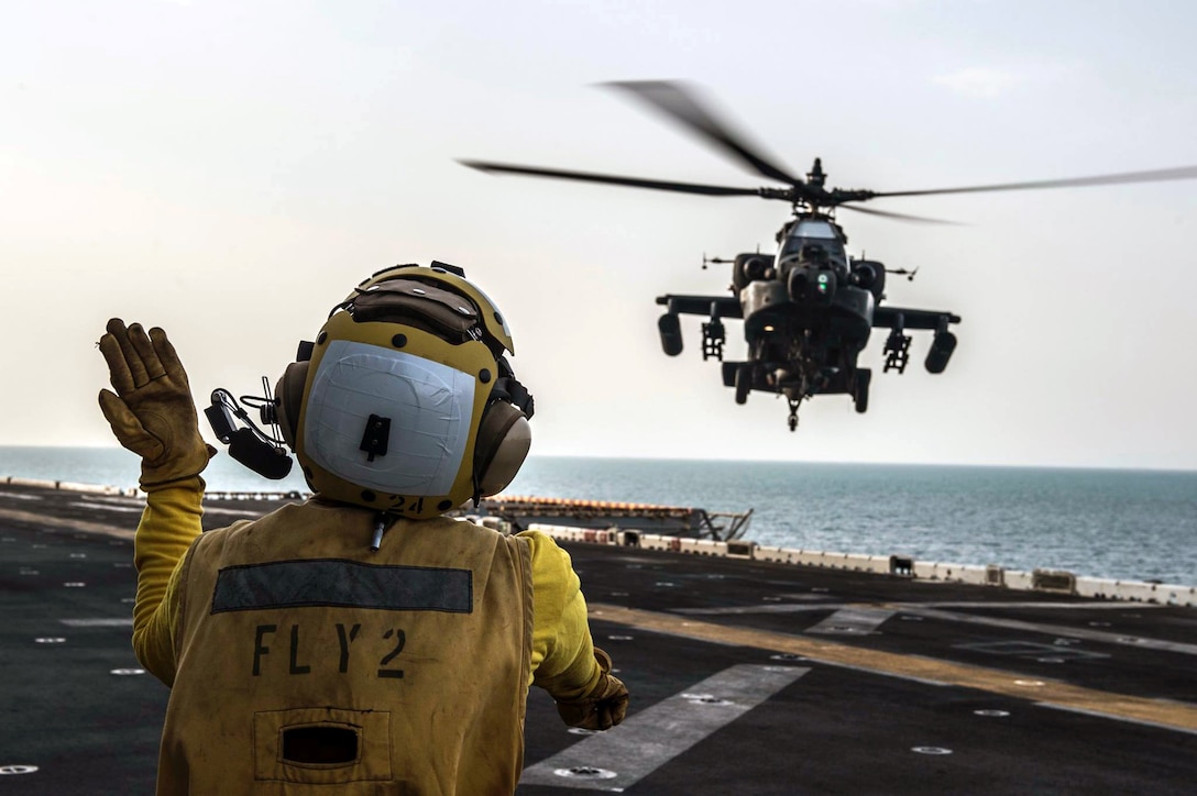 A U.S. Army AH-64 Apache helicopter pilot takes signals from a U.S. Navy seaman on the flight deck of the USS Essex during landing qualifications as part of an interoperability exercise in the Persian Gulf, Sept. 28, 2015. The seaman is assigned to the 1st Battalion, 1st Special Operations Group. U.S. Navy photo by Petty Officer 2nd Class Bradley J. Gee