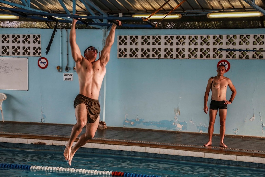 BASE AERIENNE 188, Djibouti (Sept. 22, 2015) U.S. Marine Cpl. Michael Odintz swings across monkey bars as part of an obstacle during the swim portion of the indoctrination prior to participating in a desert survival course. Odintz is a squad leader with Delta Company, Light Armored Reconnaissance Detachment, 15th Marine Expeditionary Unit. Elements of the 15th MEU are training with the 5th RIAOM in Djibouti in order to improve interoperability between the MEU and the French military. (U.S. Marine Corps photo by Sgt. Steve H. Lopez/Released)
